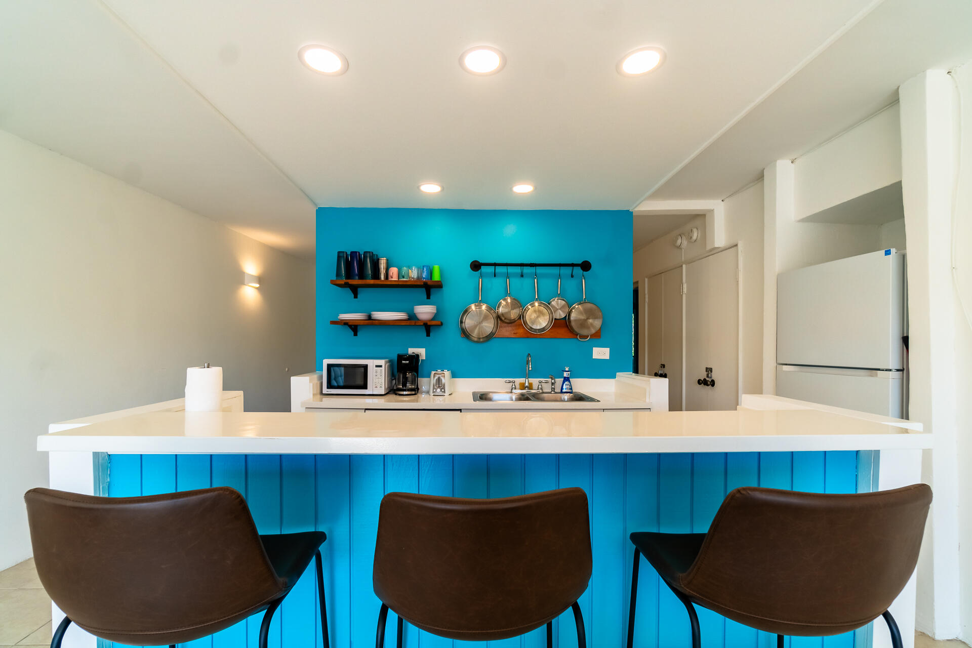 Kitchen with a turquoise island and accent wall, three brown stools, and hanging cookware.
