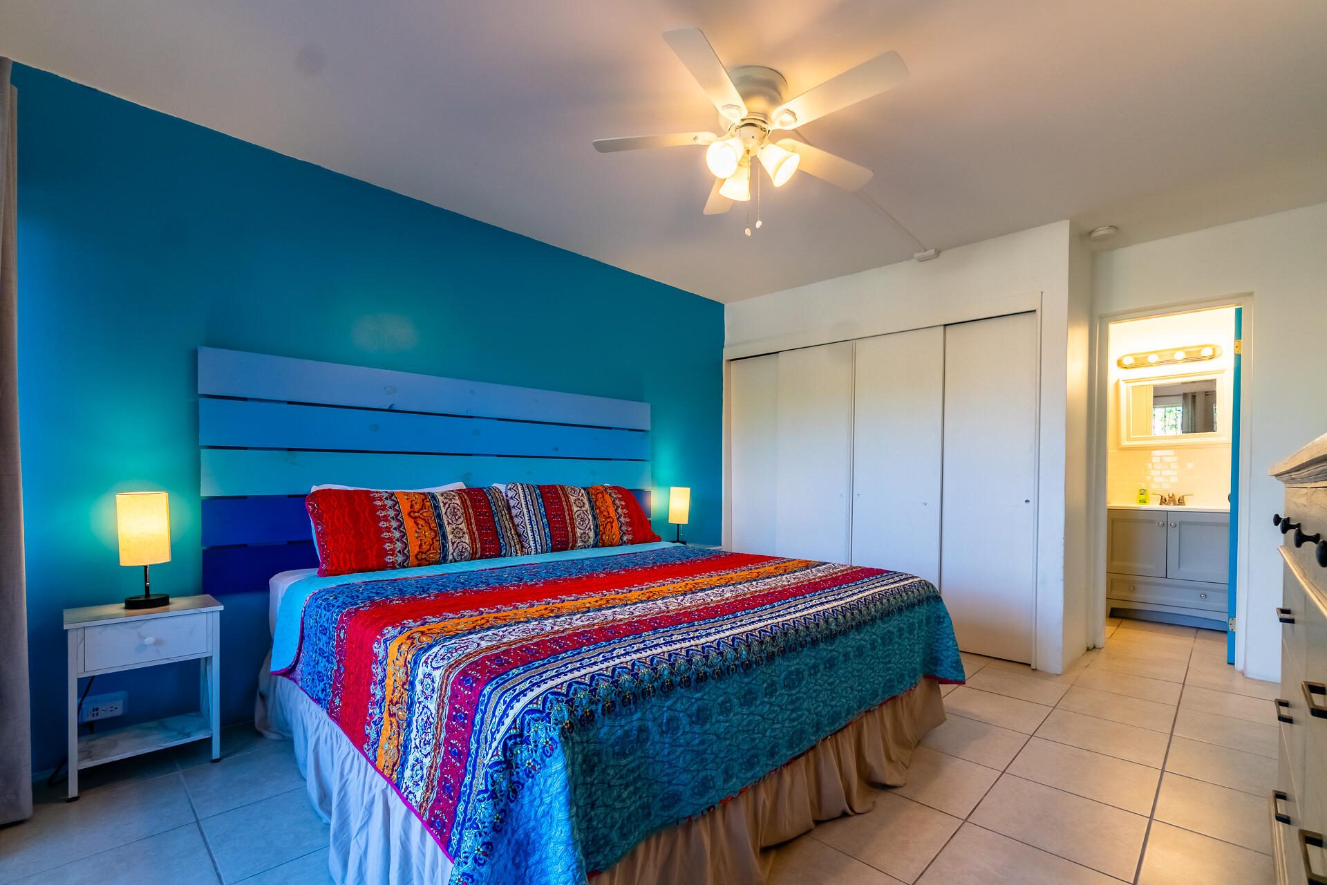 Bedroom with a colorful patterned bedspread, teal accent wall, and doorway to a bathroom.