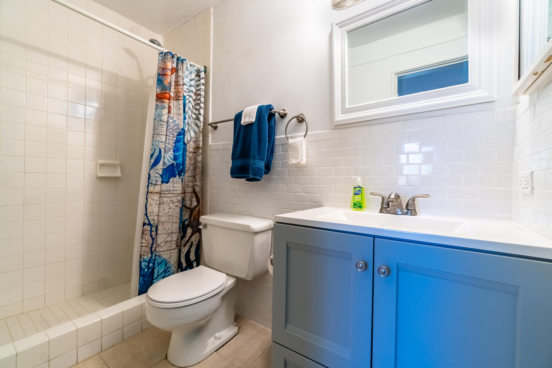 Bathroom with a blue vanity, white tiled shower, and patterned blue shower curtain.