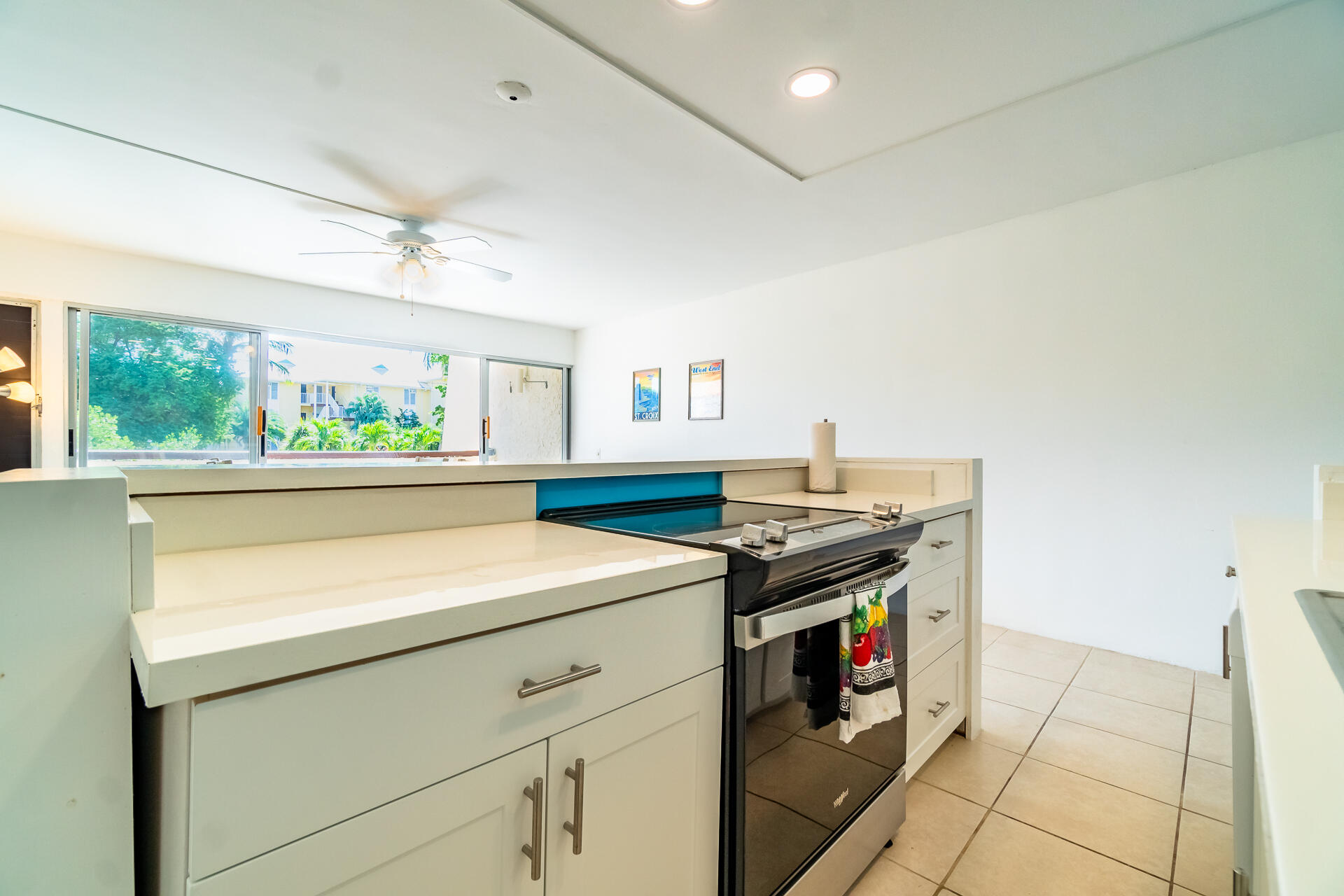 Kitchen with white cabinetry, a black electric range, and a wide window overlooking tropical greenery.