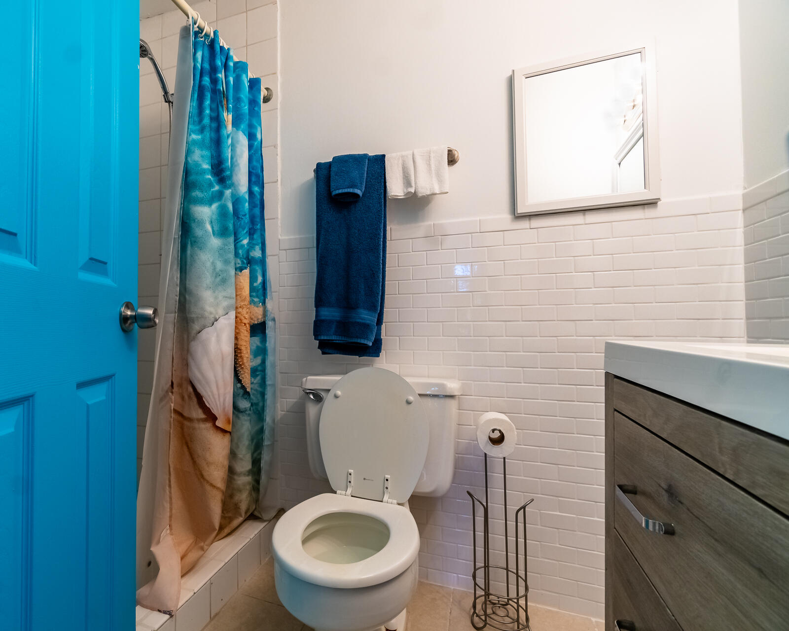 Bathroom with a colorful shower curtain, white tile, and bright blue door.