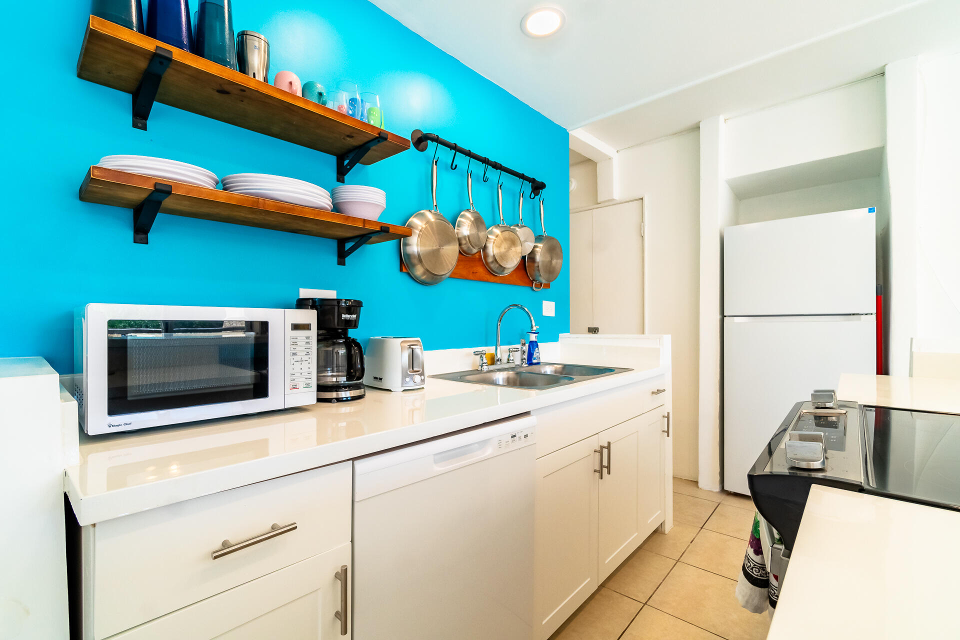 Kitchen with turquoise walls, open wooden shelves, hanging pans, and white cabinets.