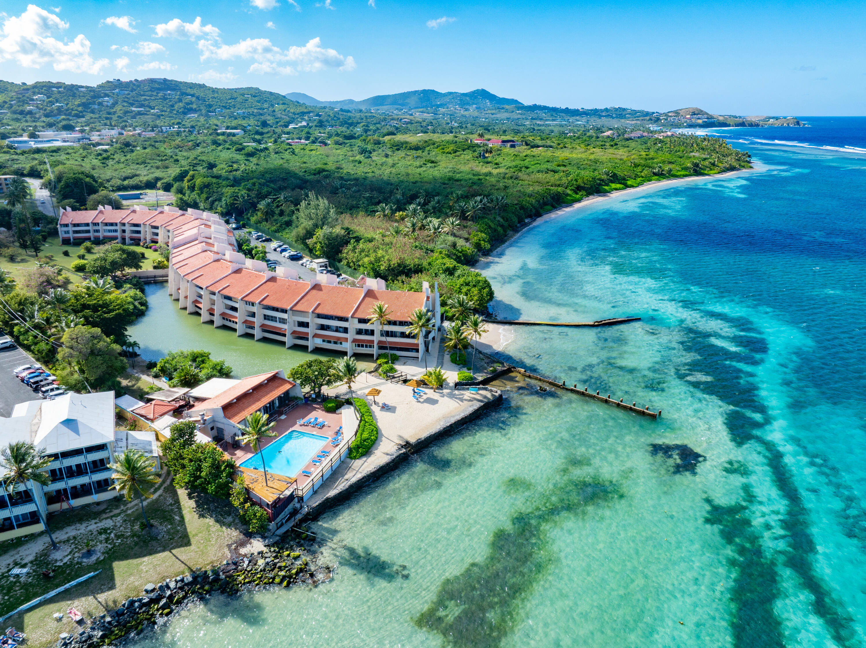 Waterfront condominium complex beside turquoise water, with a pool and terracotta roofs.