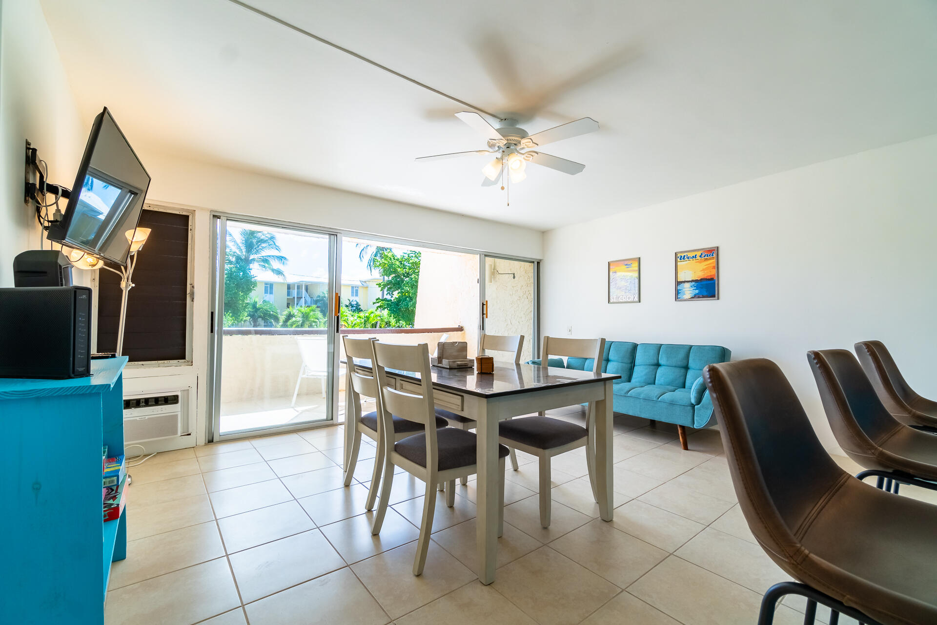 Furnished dining and living area with a turquoise sofa and sliding doors to a leafy balcony.