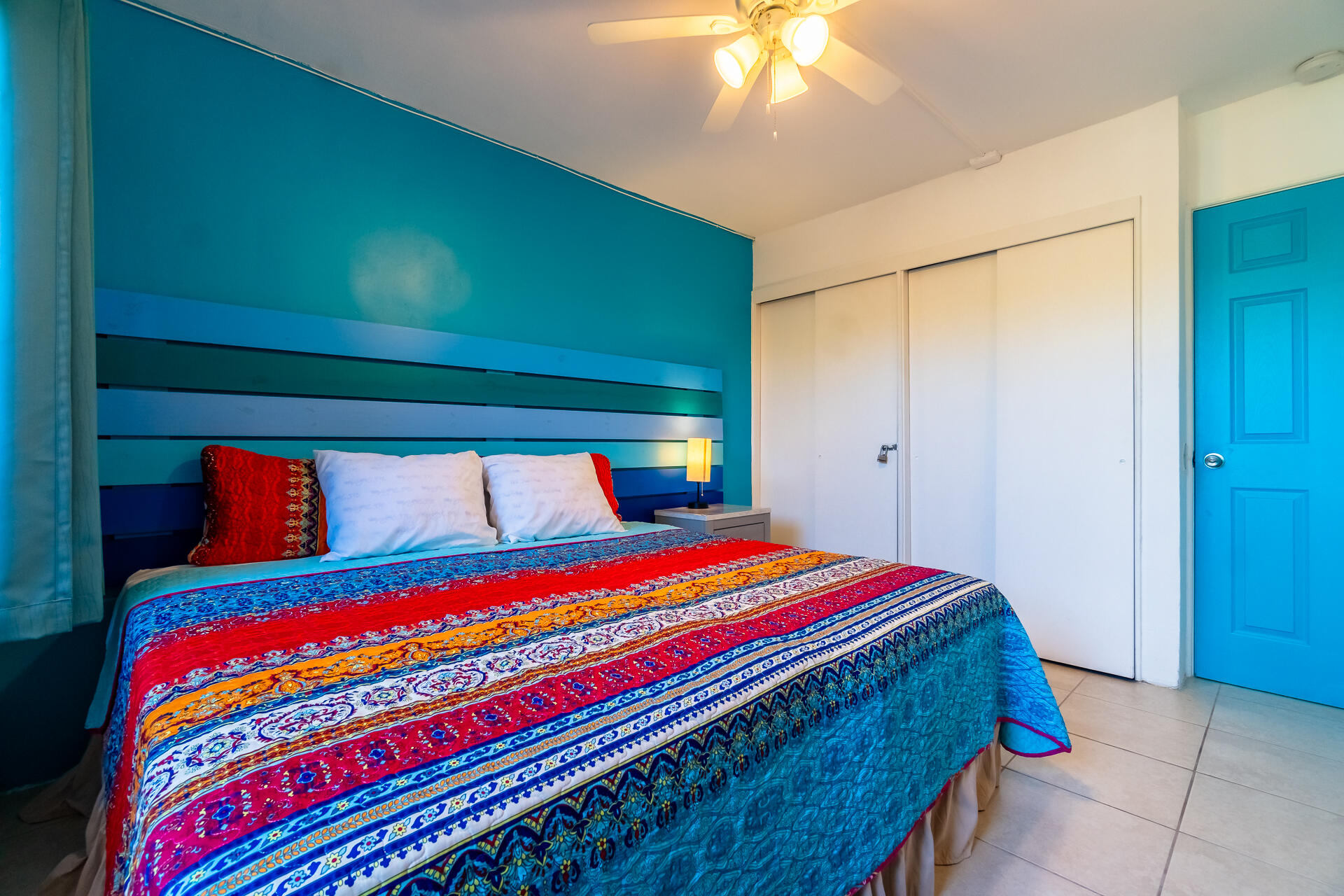 Bedroom with a colorful patterned bedspread, teal accent wall, and white sliding closet doors.