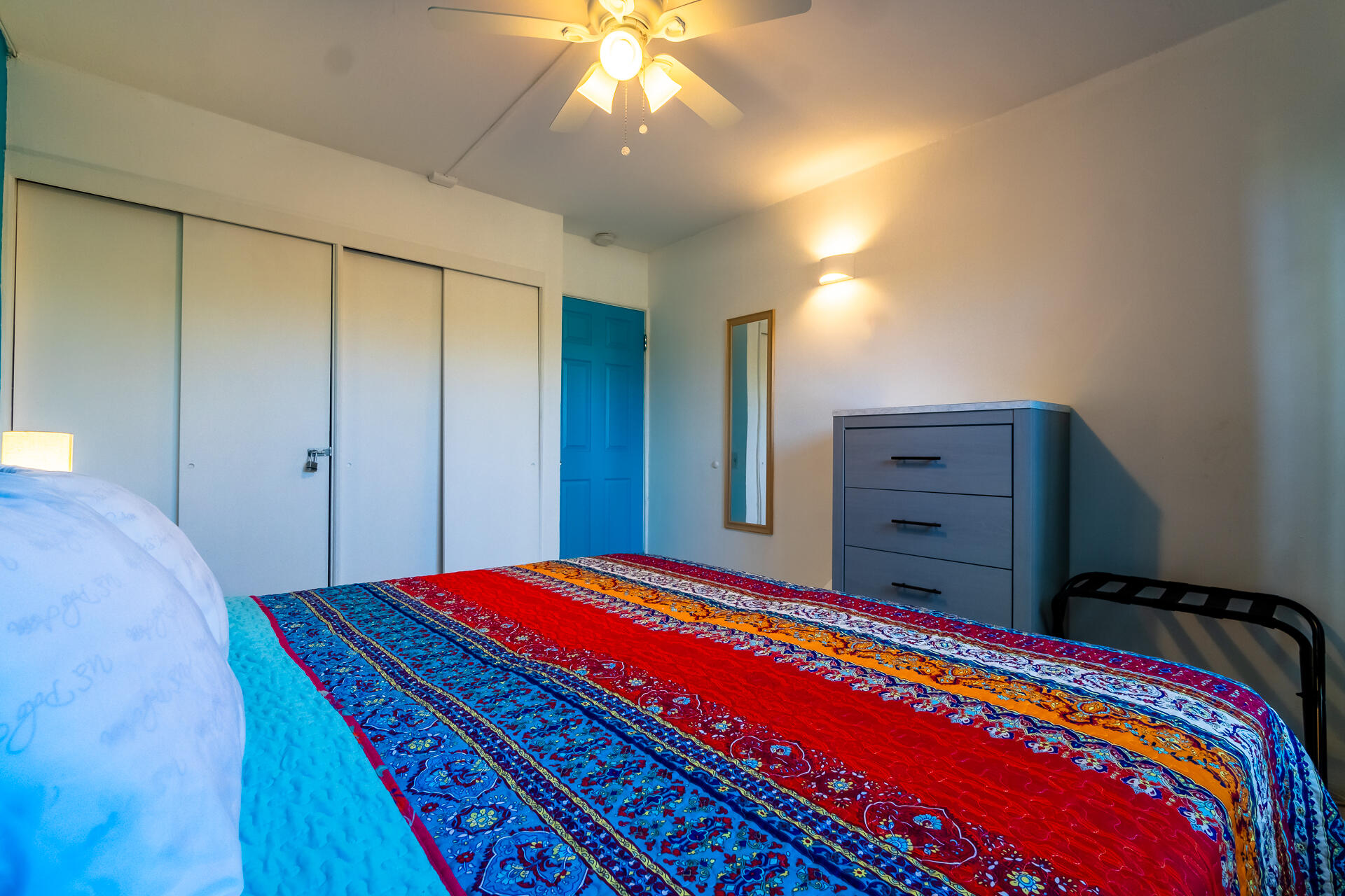 Bedroom with a vivid red, blue, and orange patterned quilt, sliding closets, and a blue door.