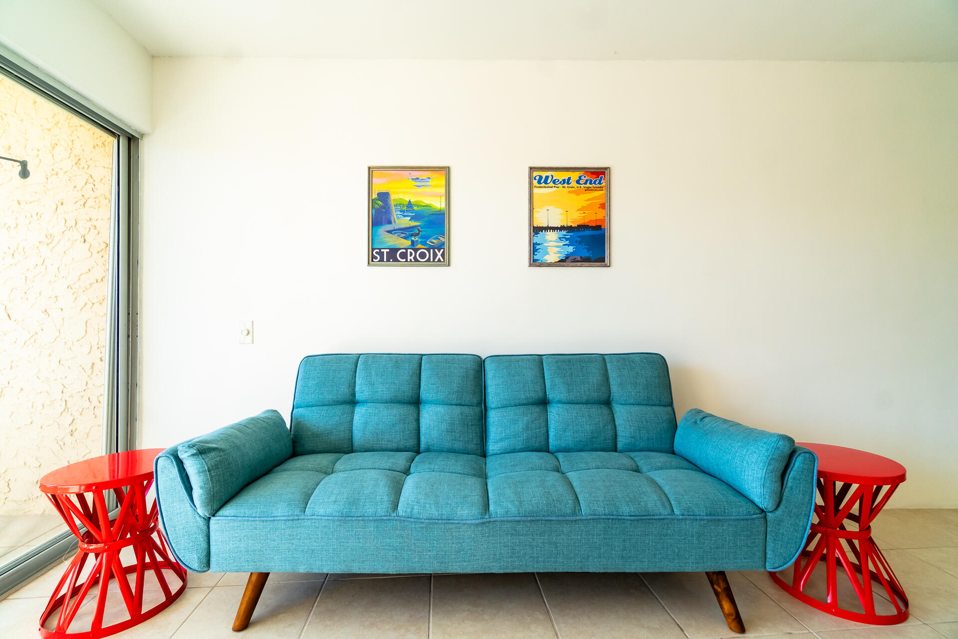 Living room with a turquoise sofa, red side tables, and framed St. Croix posters.