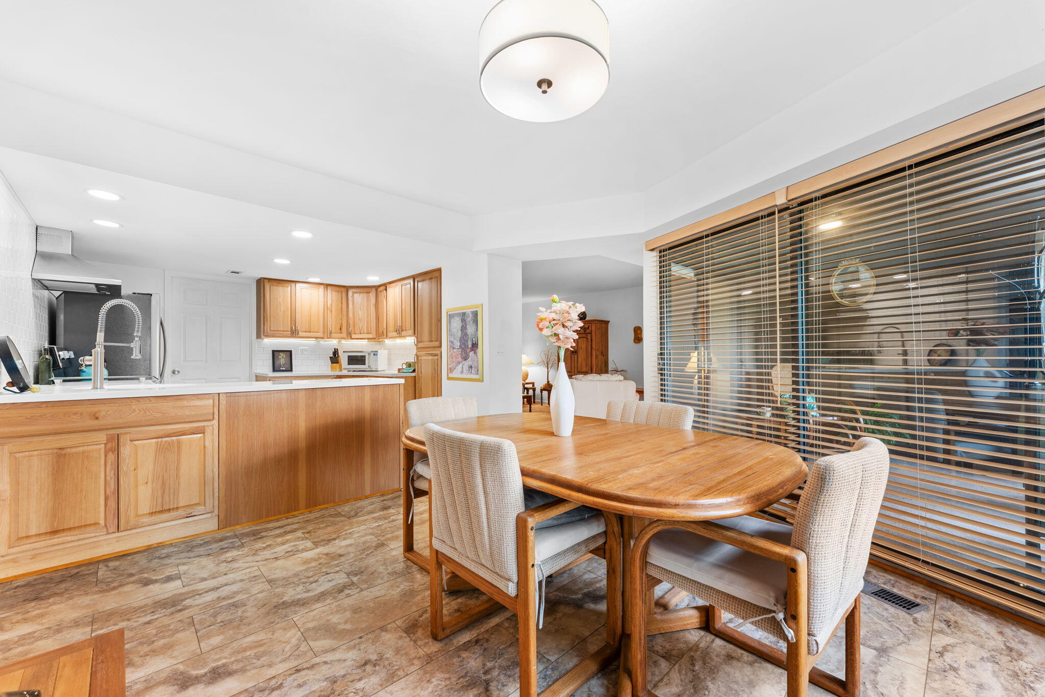 Kitchen and dining area with honey-toned cabinets, a wooden table, and wide windows with blinds.
