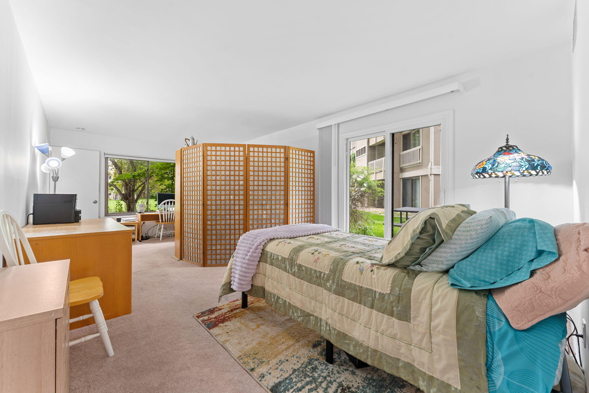 Furnished bedroom with a wooden folding screen and sliding glass doors overlooking a grassy courtyard.