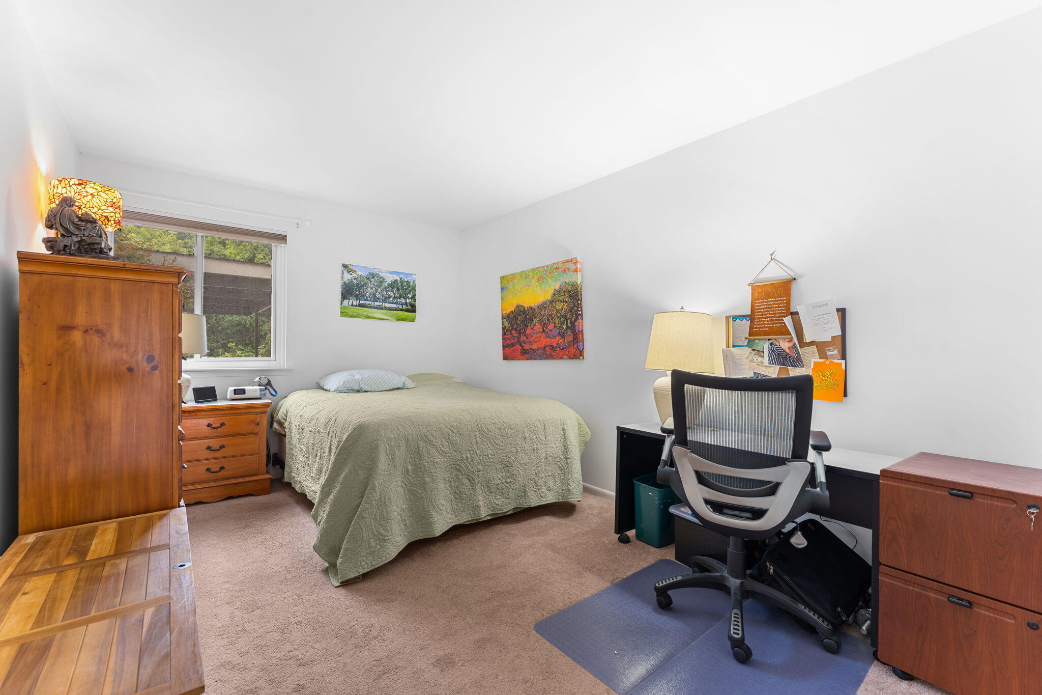 Bedroom with a pale green quilted bed, wooden dresser, and desk with an office chair.
