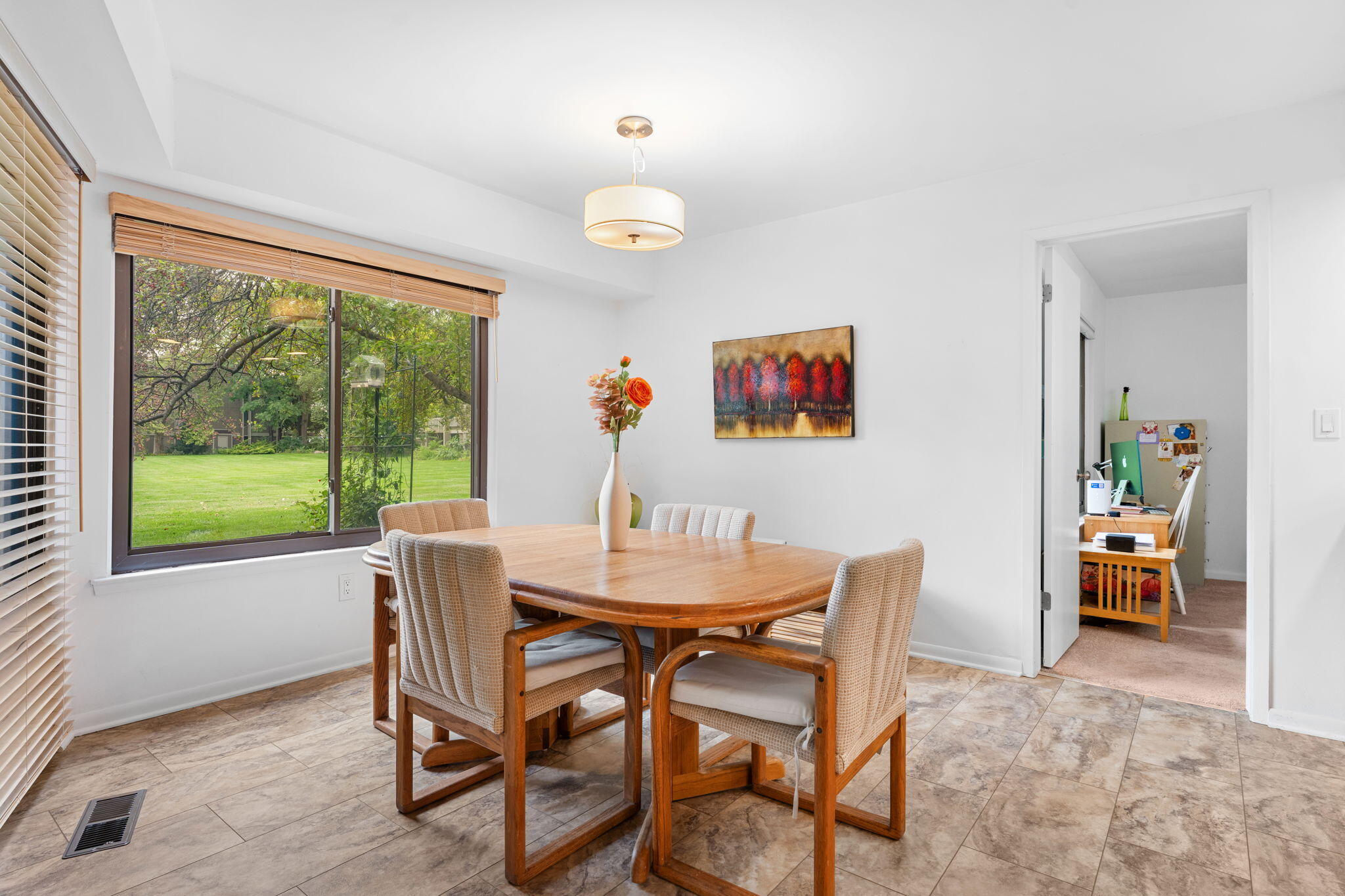 Dining room with a wooden table and chairs beside a large window overlooking a green lawn.