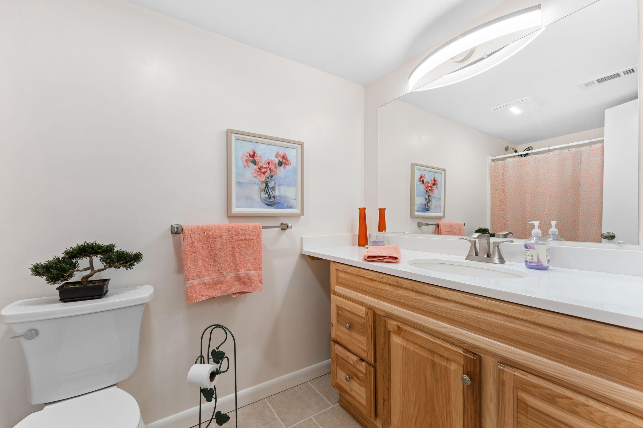 Bathroom with a wood vanity, large mirror, and coral towels.
