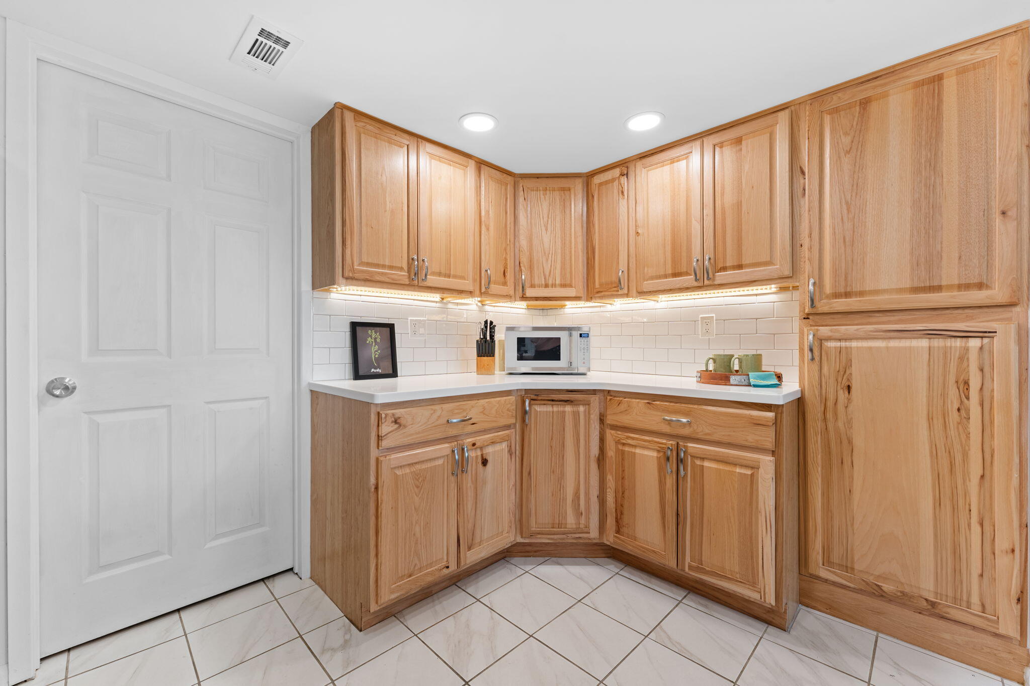 Kitchen with honey-colored wood cabinets, white tile backsplash, and a built-in microwave.
