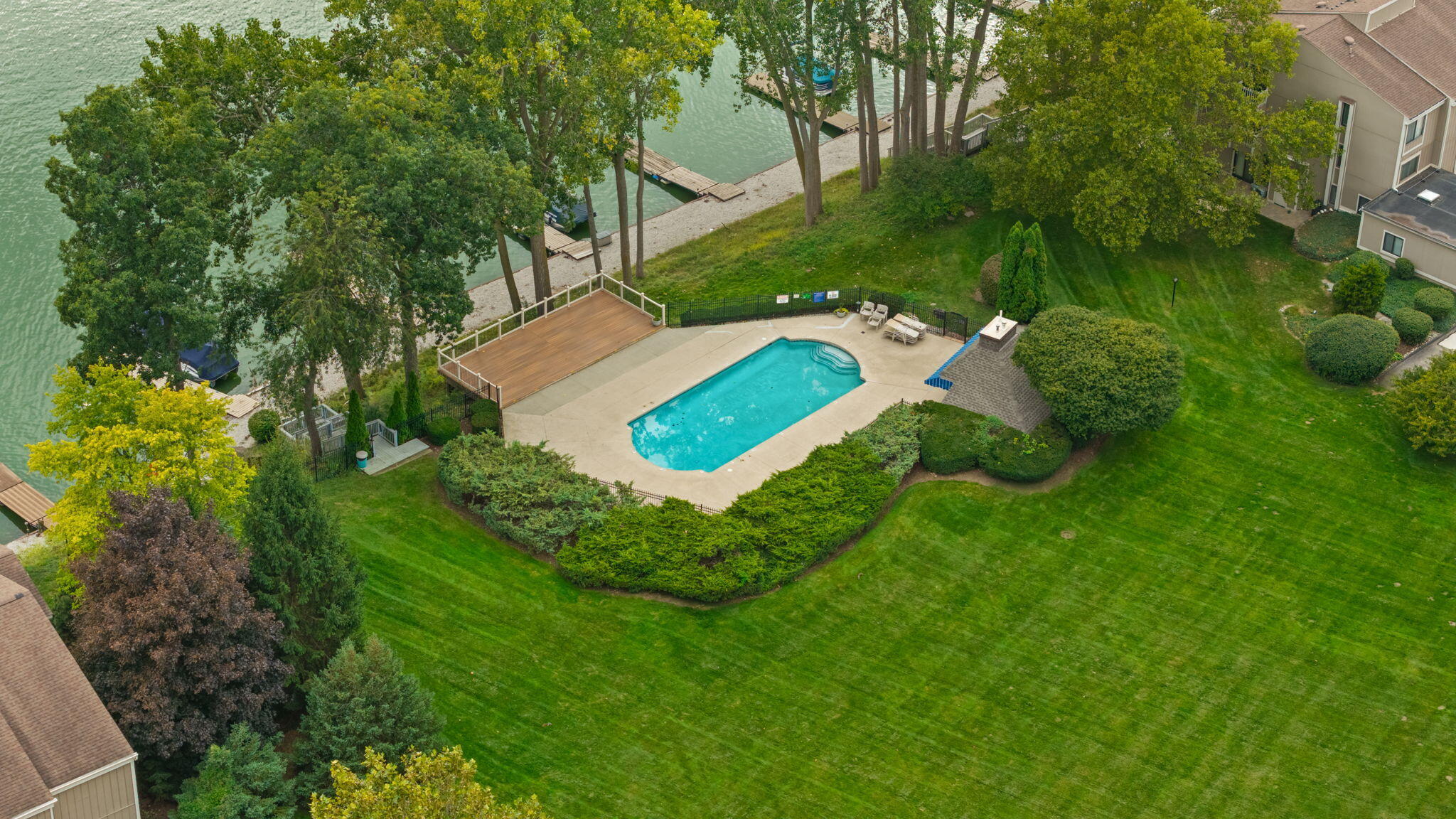 Aerial view of a condominium pool and deck beside a tree-lined waterfront.