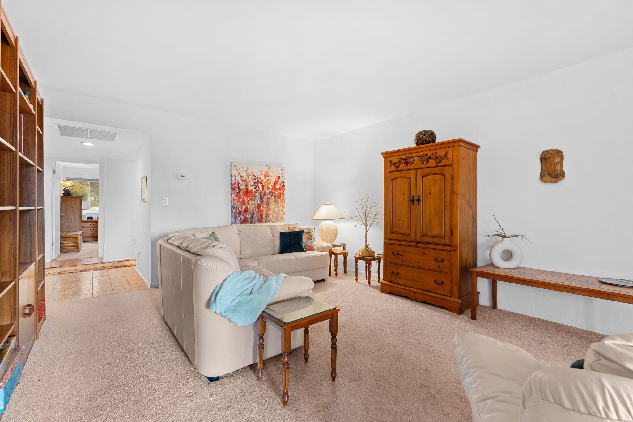 Furnished living room with a light sectional, wooden cabinet, and colorful abstract artwork.