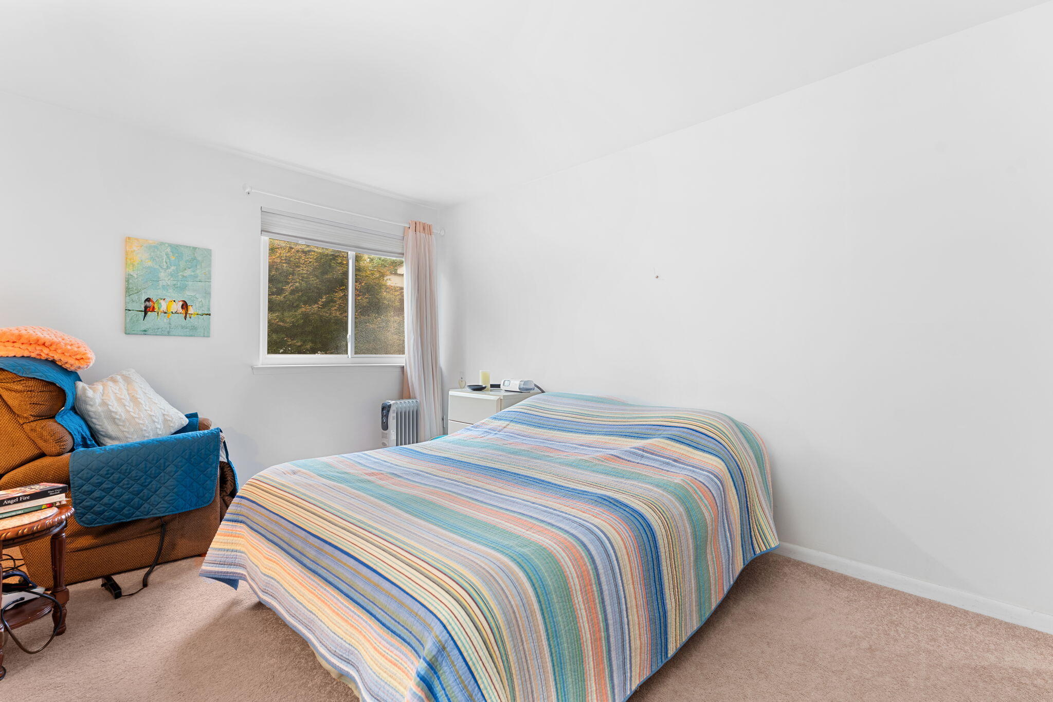 Bedroom with a colorful striped quilt on the bed and a brown armchair beside the window.