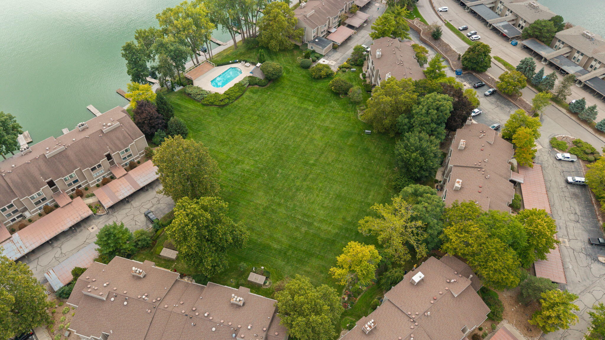 Aerial view of lakeside condominiums with a central lawn and outdoor pool.