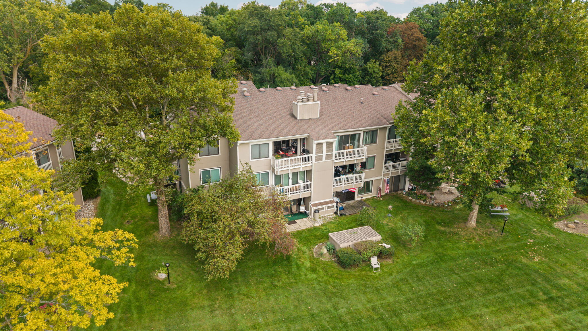 Aerial view of condominiums with white balconies, a landscaped lawn, and mature trees.