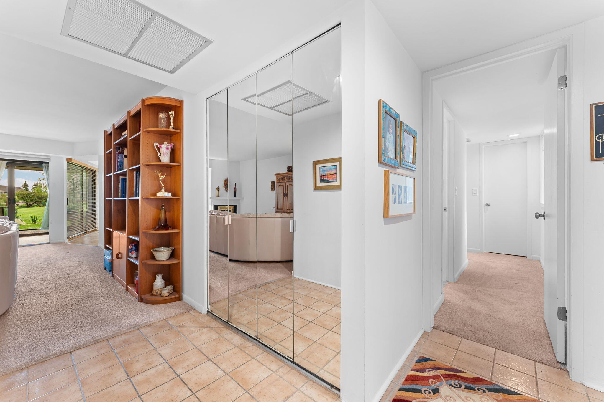 Home entry with mirrored closet doors, tile flooring, wooden display shelves, and a carpeted hallway.
