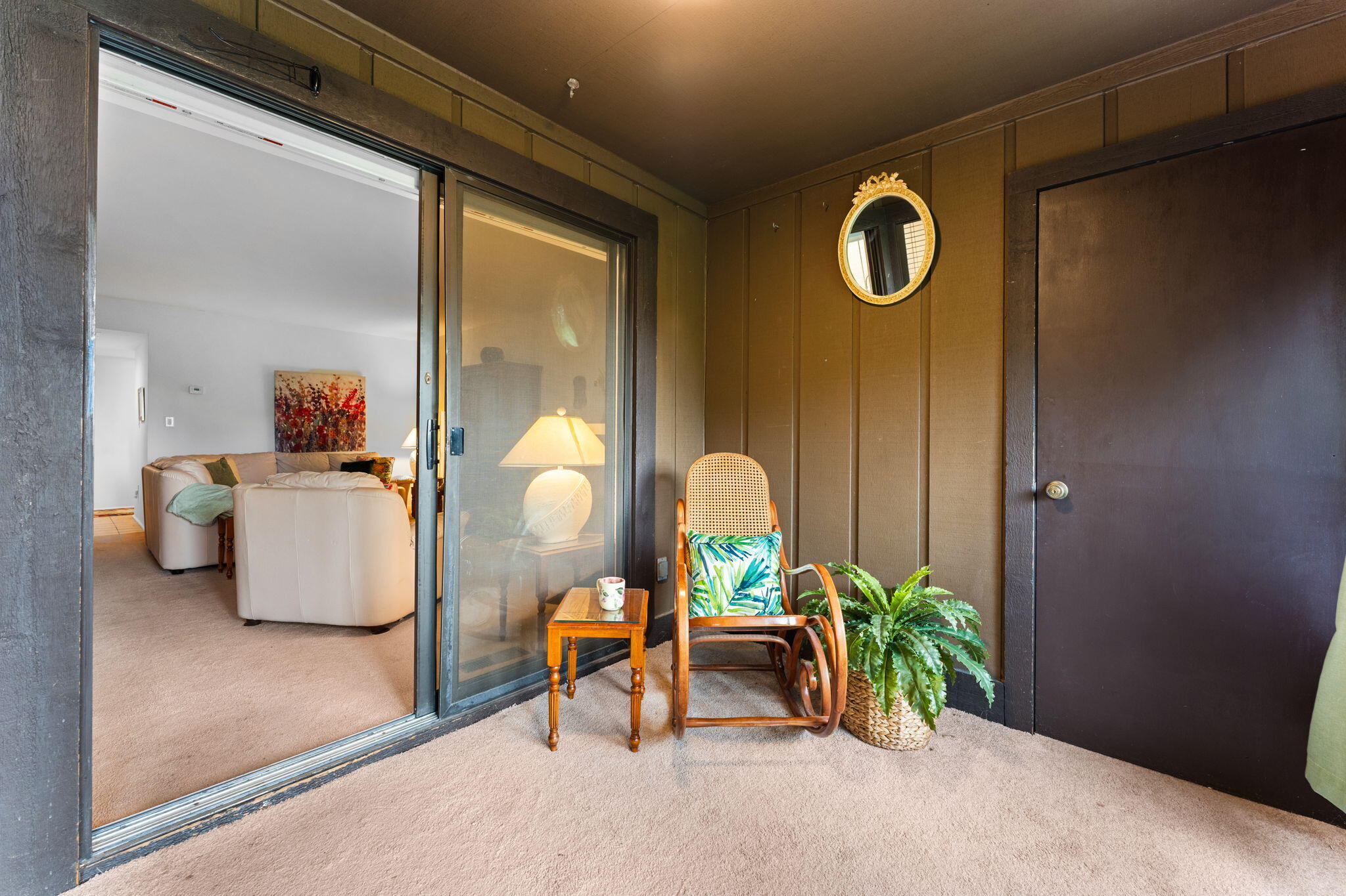 Enclosed balcony with a cane chair, side table, potted fern, and sliding glass door to the living room.