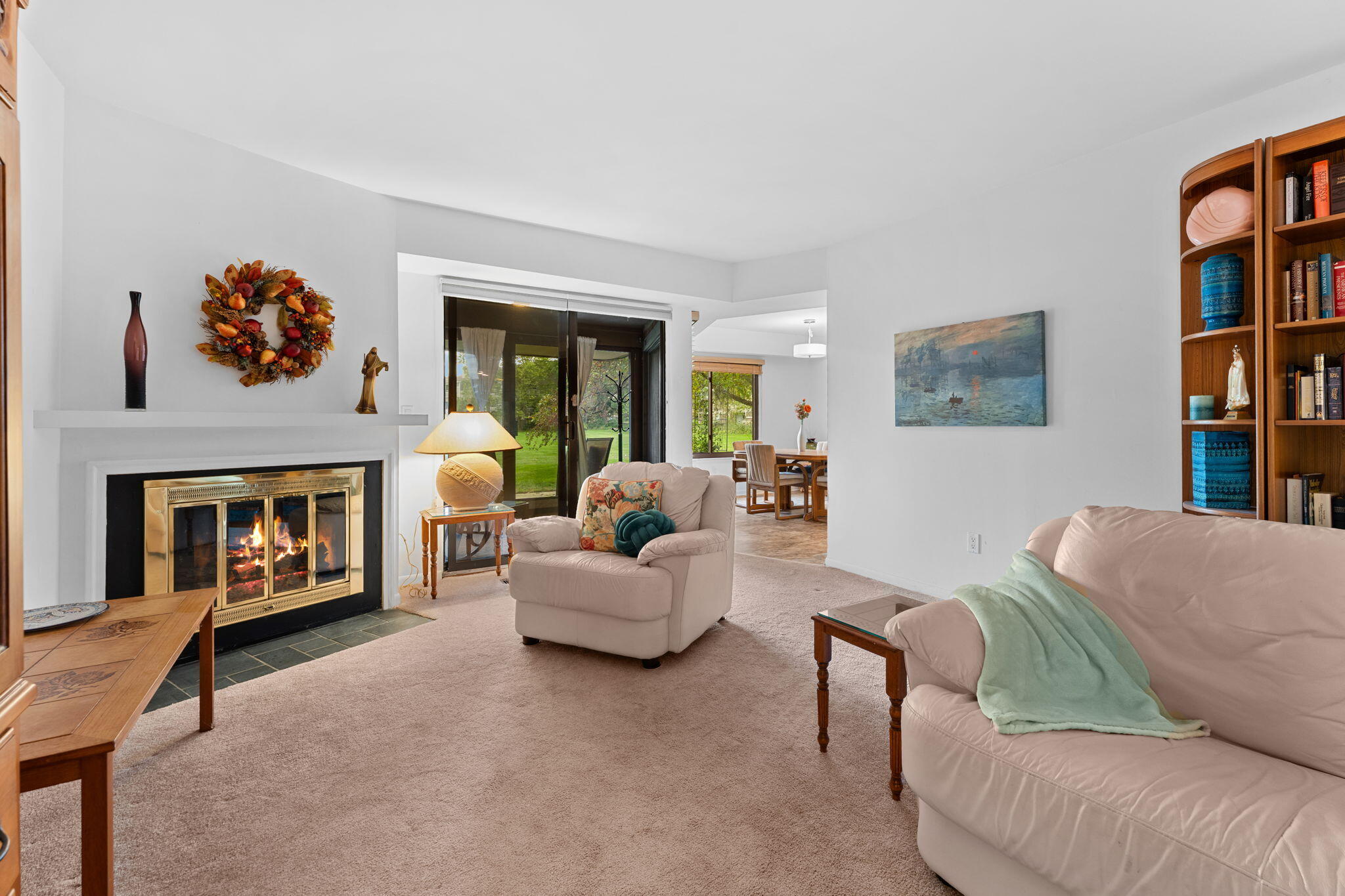 Living room with a lit fireplace, pale sofas, and sliding glass doors overlooking a lawn.
