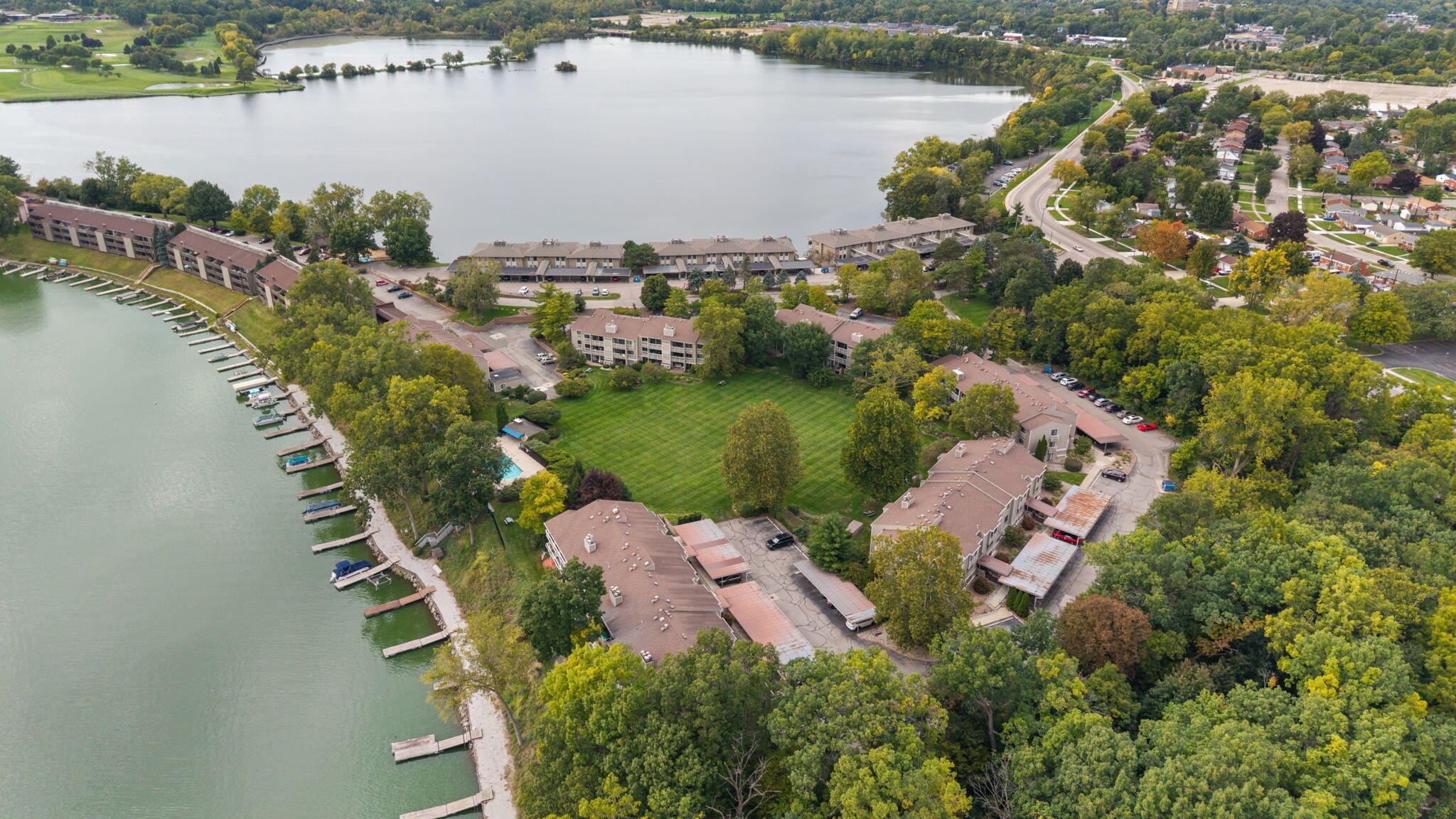Aerial view of lakeside condominiums with shoreline docks, a broad lawn, and wooded surroundings.