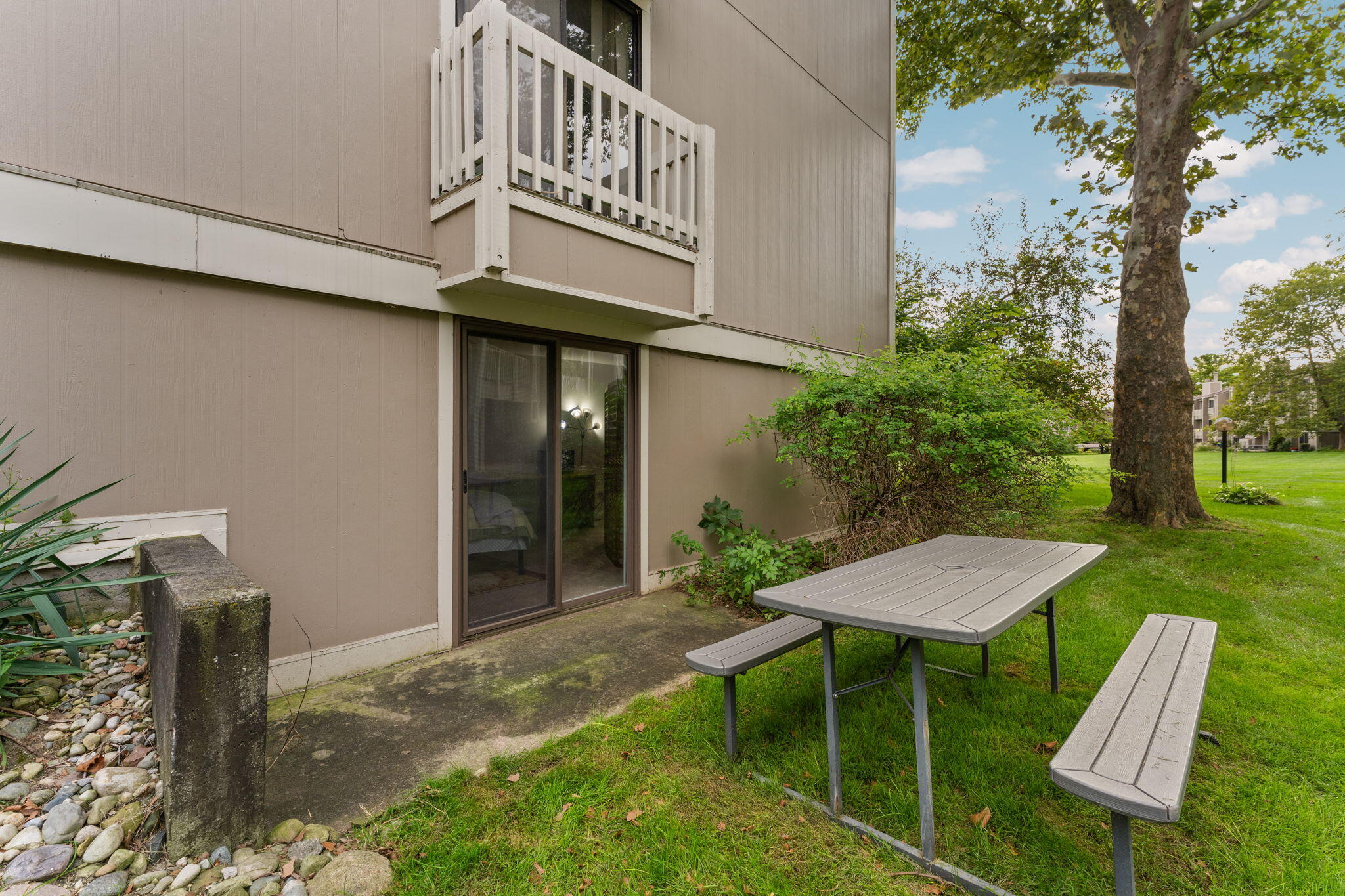 Condominium patio with a picnic table, upper balcony, and lawn shaded by a mature tree.