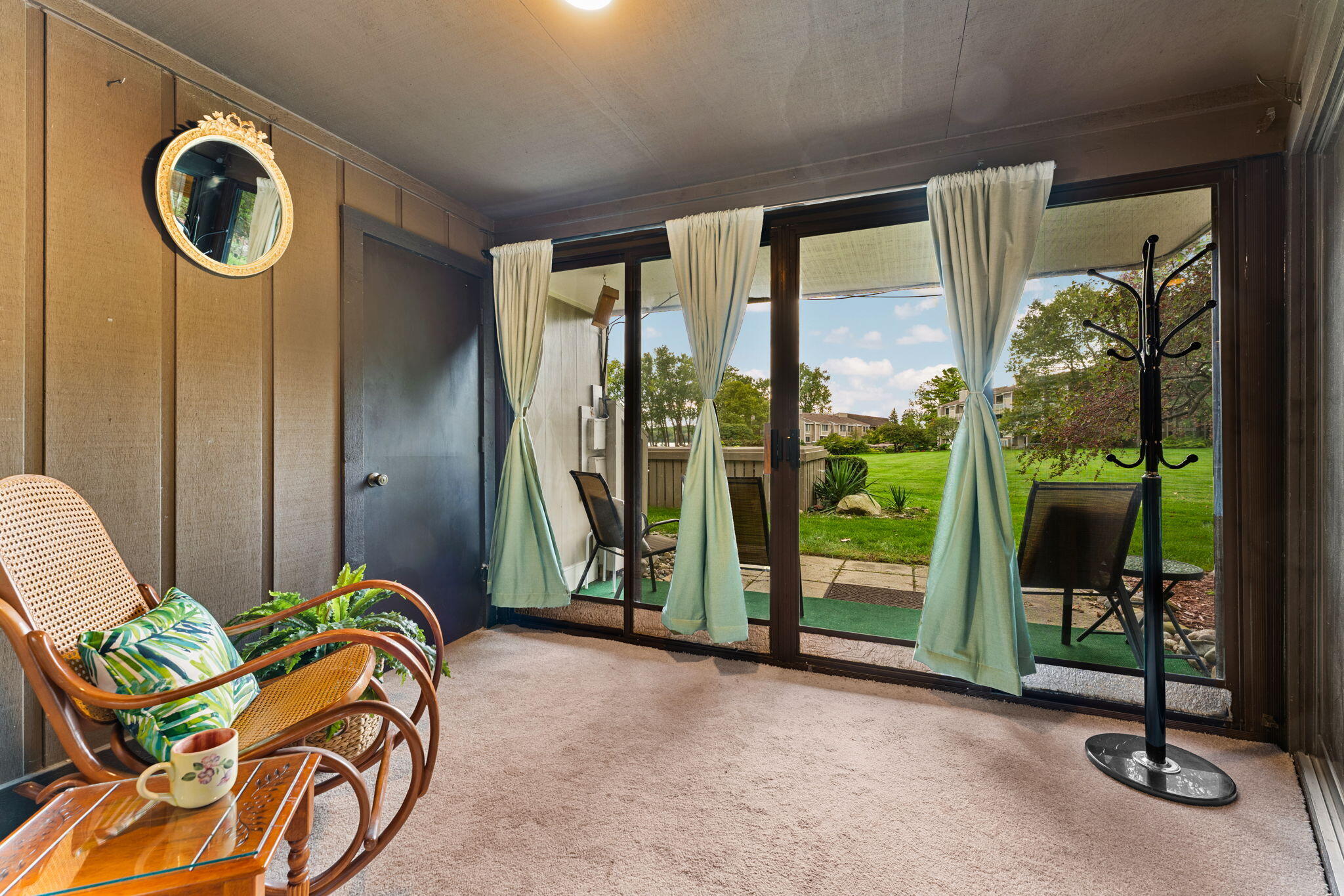 Furnished sunroom with wicker chairs and sliding glass doors overlooking a patio and green lawn.