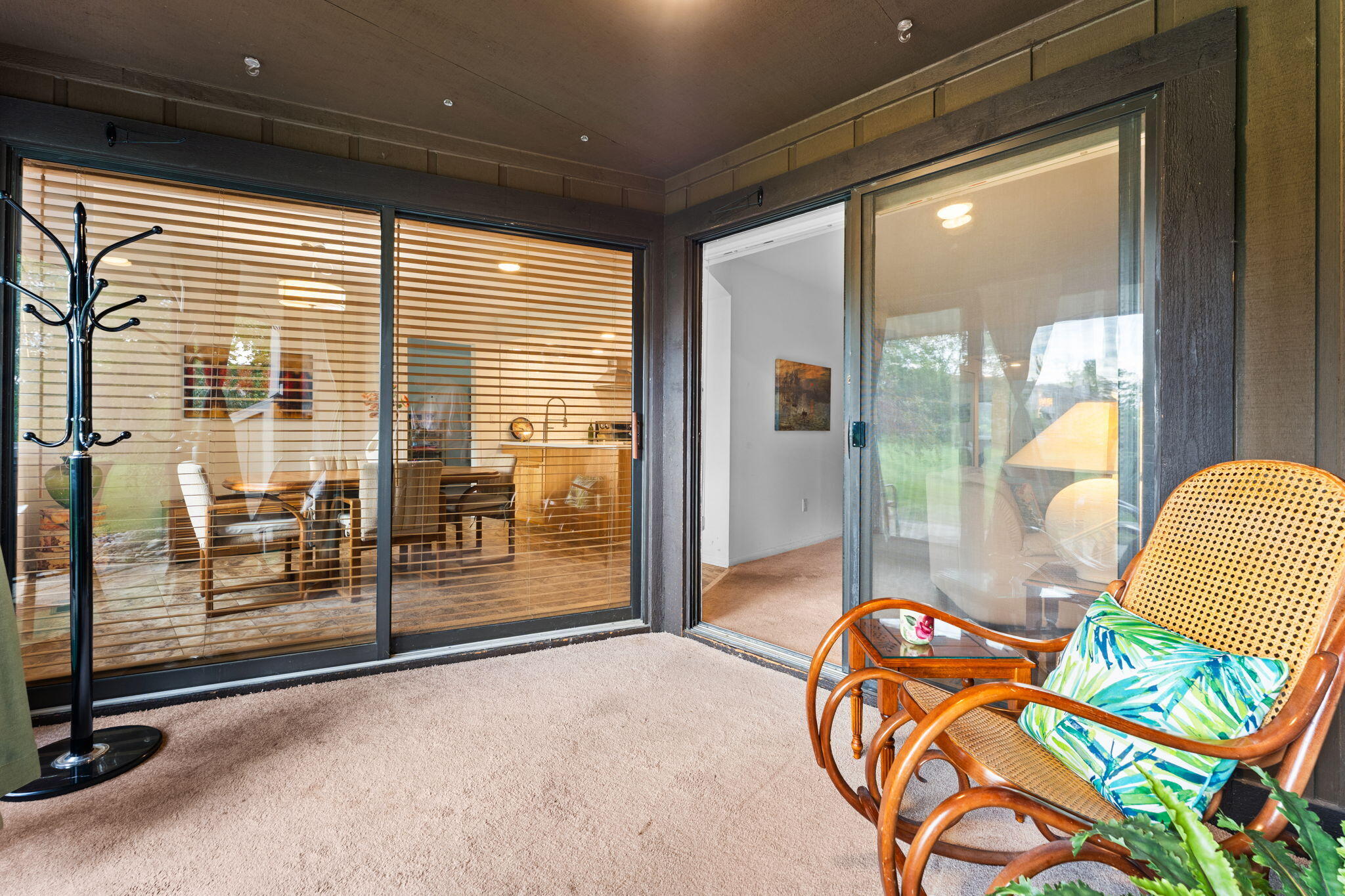 Carpeted sunroom with sliding glass doors, wicker chairs, and a view into the dining area and kitchen.