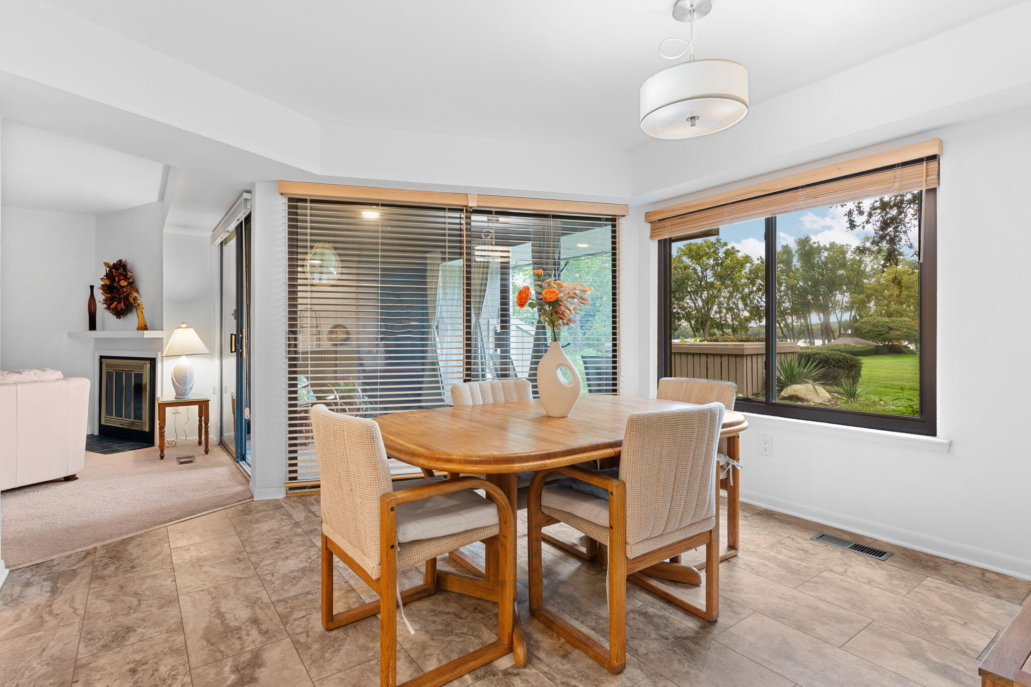 Dining area with a wooden table, woven chairs, and large windows overlooking trees and water.
