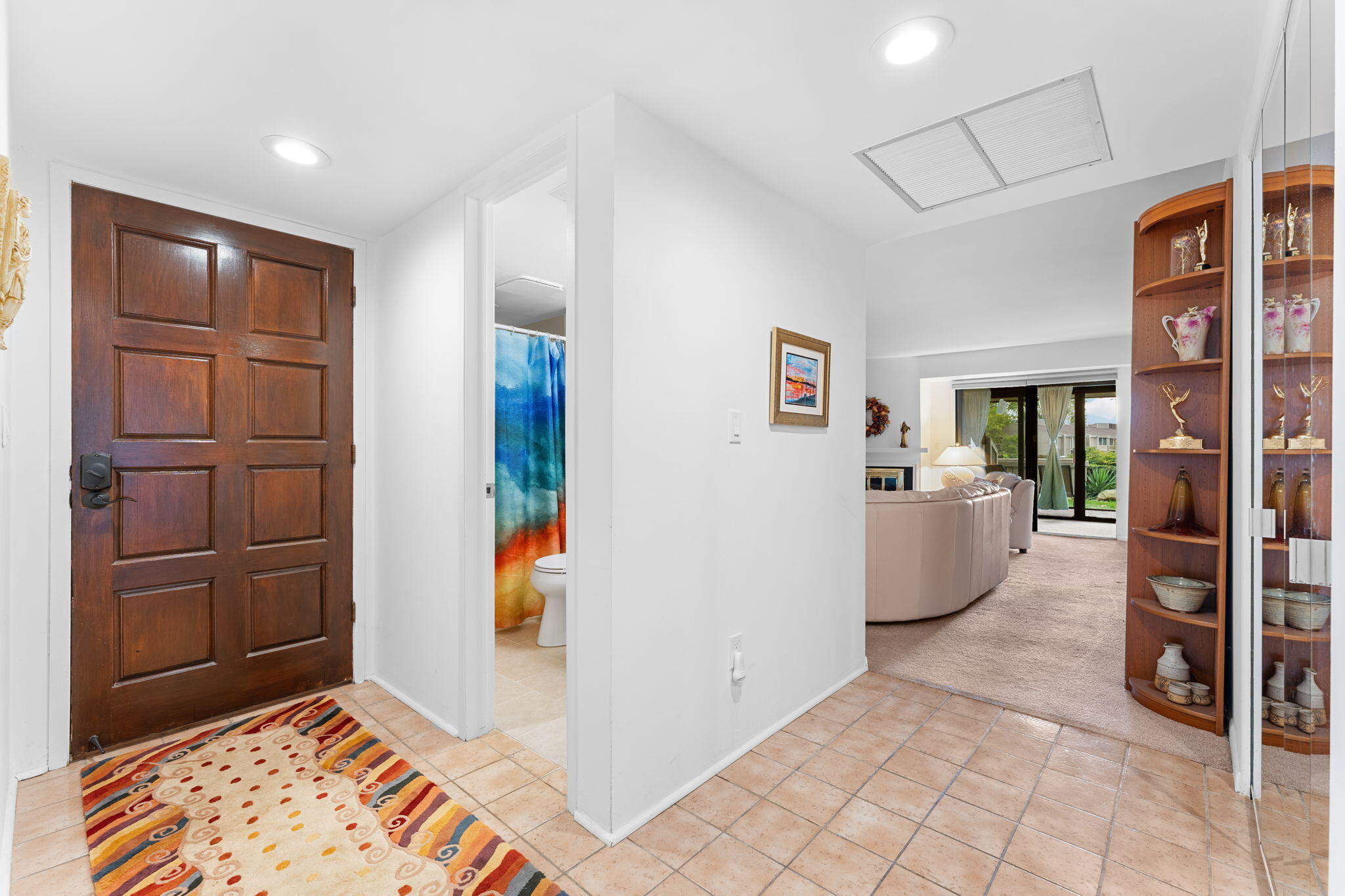 Condo entry foyer with dark wood door, tiled floor, patterned rug, and view into the living room.