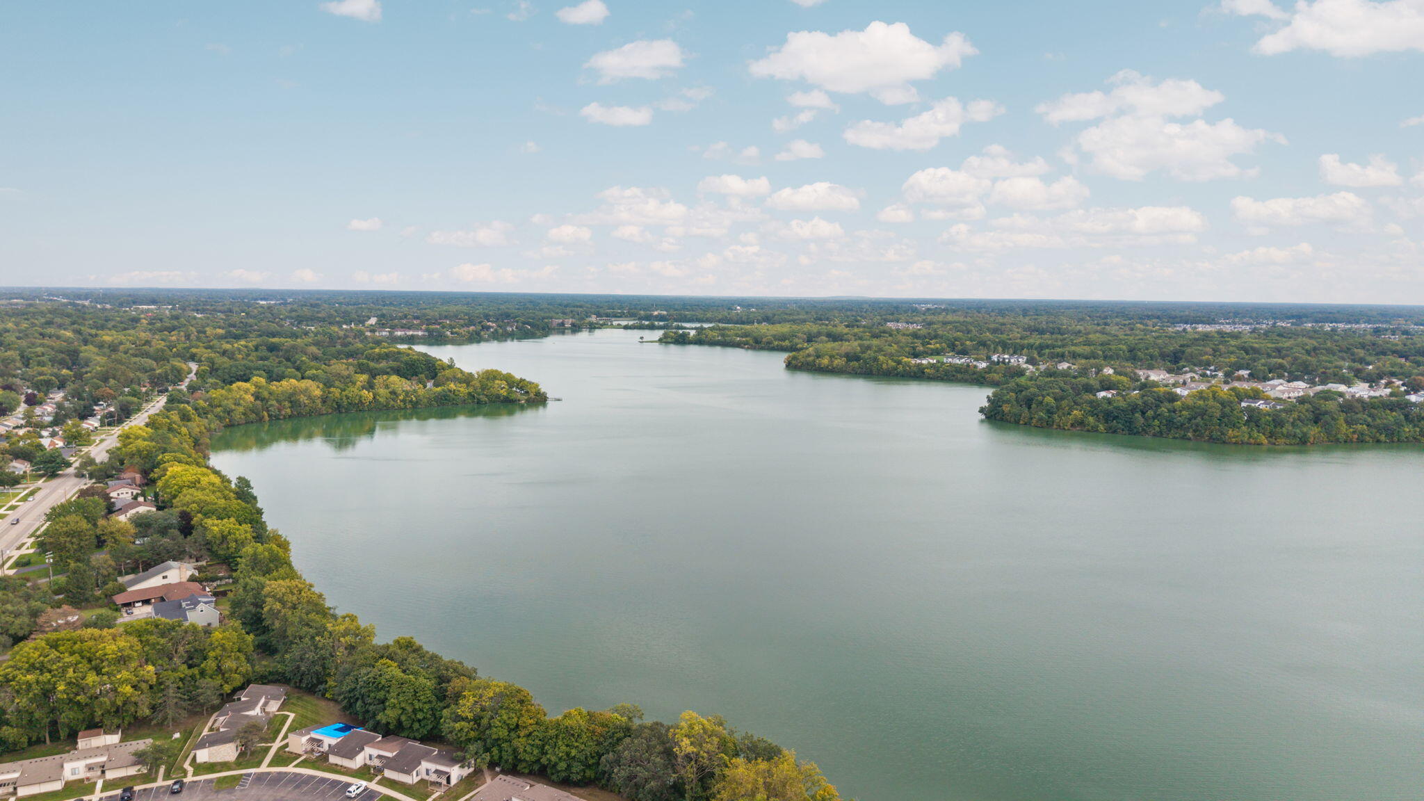 Aerial view of a broad lake bordered by wooded neighborhoods and homes.