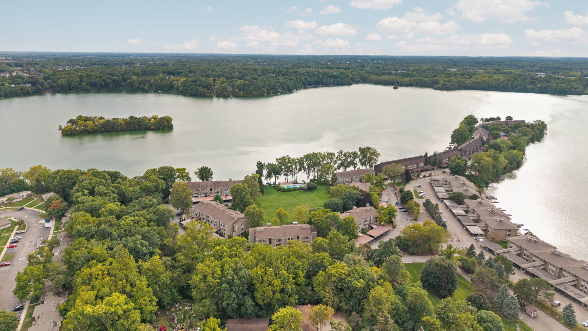 Aerial view of lakefront condominiums, with a wooded shoreline, small island, and lakeside pool.