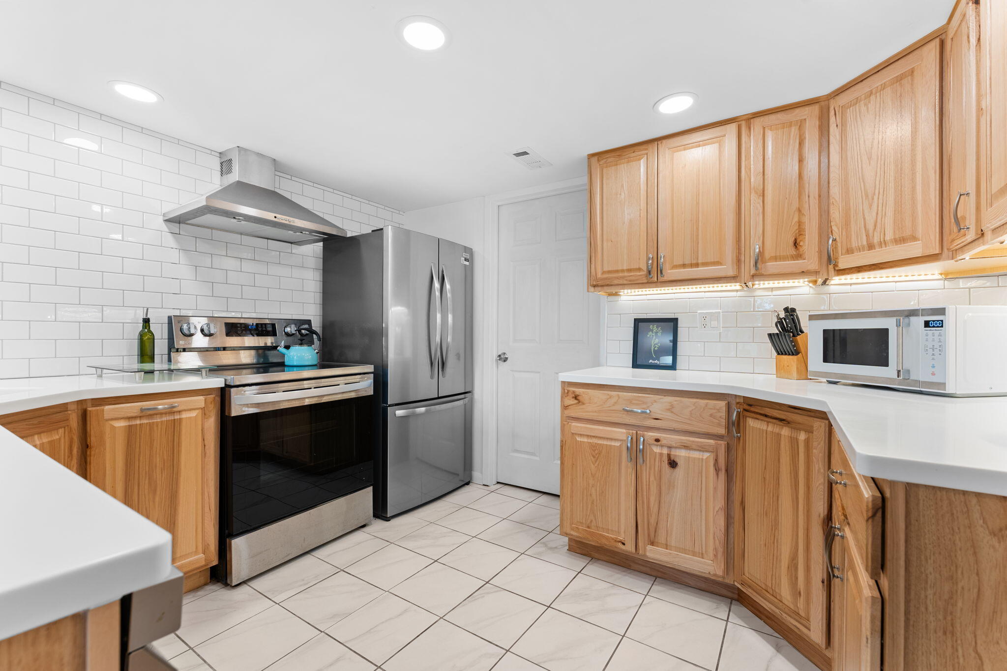 Kitchen with natural wood cabinets, white tile backsplash, and stainless steel appliances.