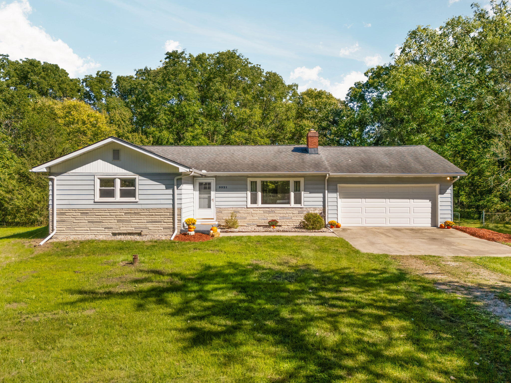 Single-story gray house with stone veneer, a two-car garage, and a tree-lined lawn.
