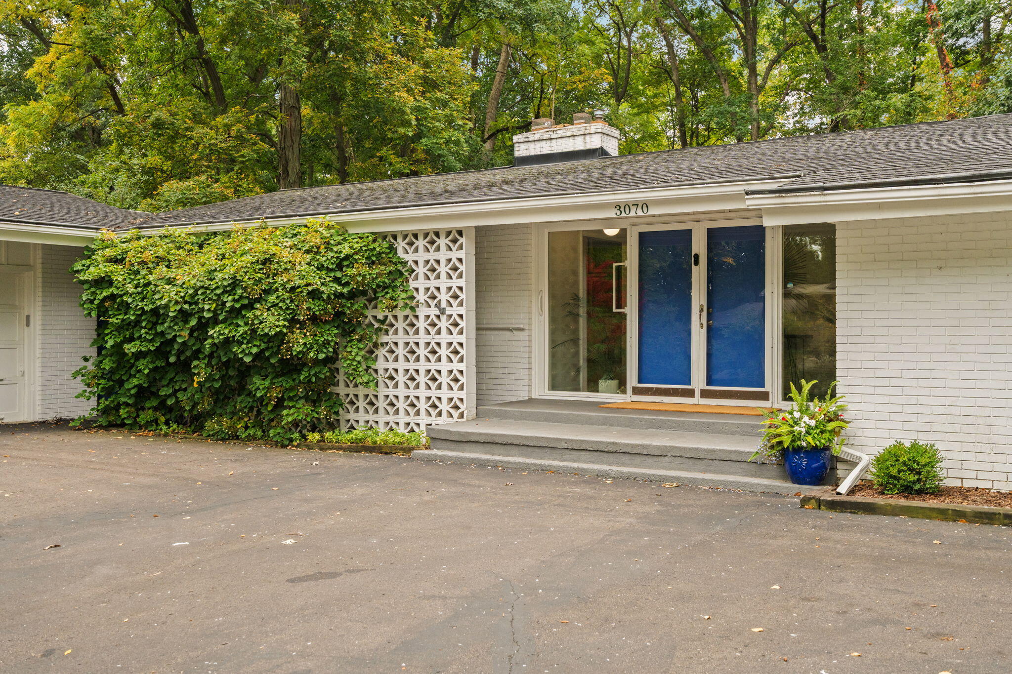 White brick house with blue double doors, a breeze-block screen, and mature trees.