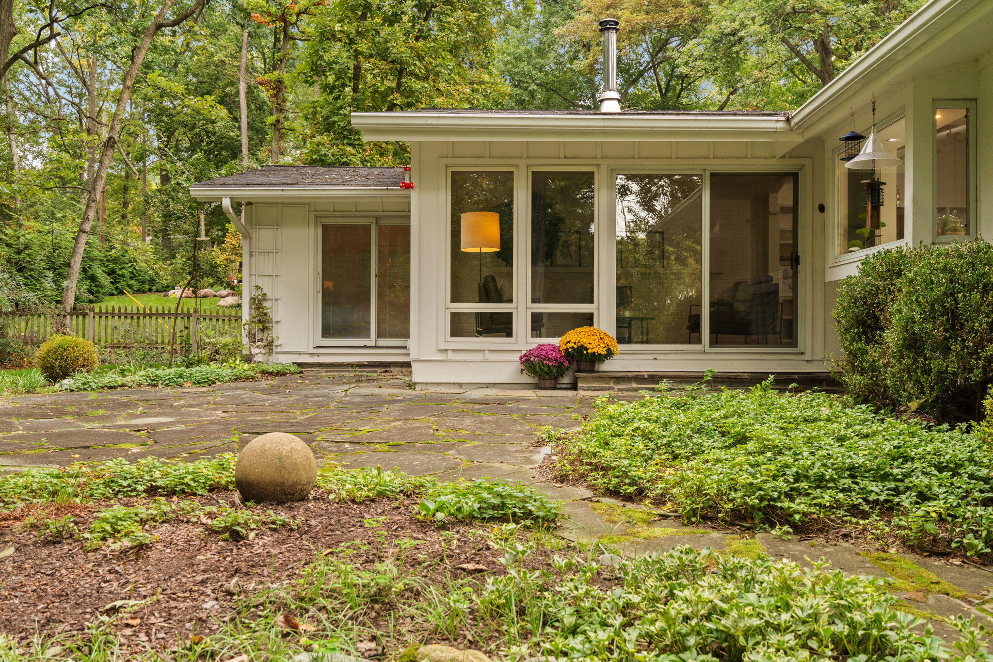 Home's rear exterior with broad windows, a stone patio, and a leafy garden.