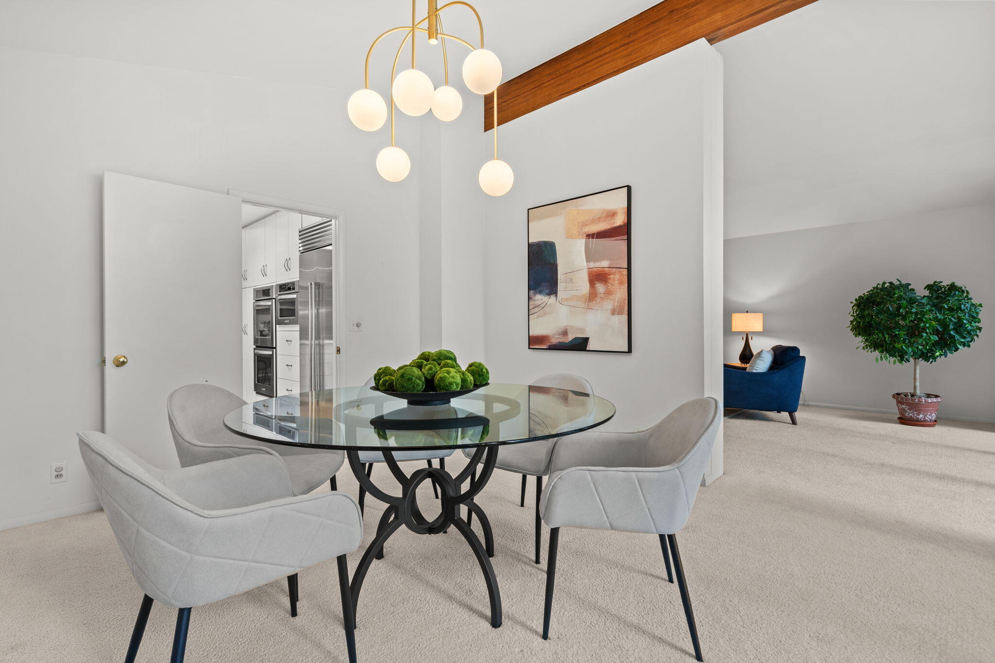 Dining room with a glass table, pale chairs, globe chandelier, and exposed wood ceiling beam.
