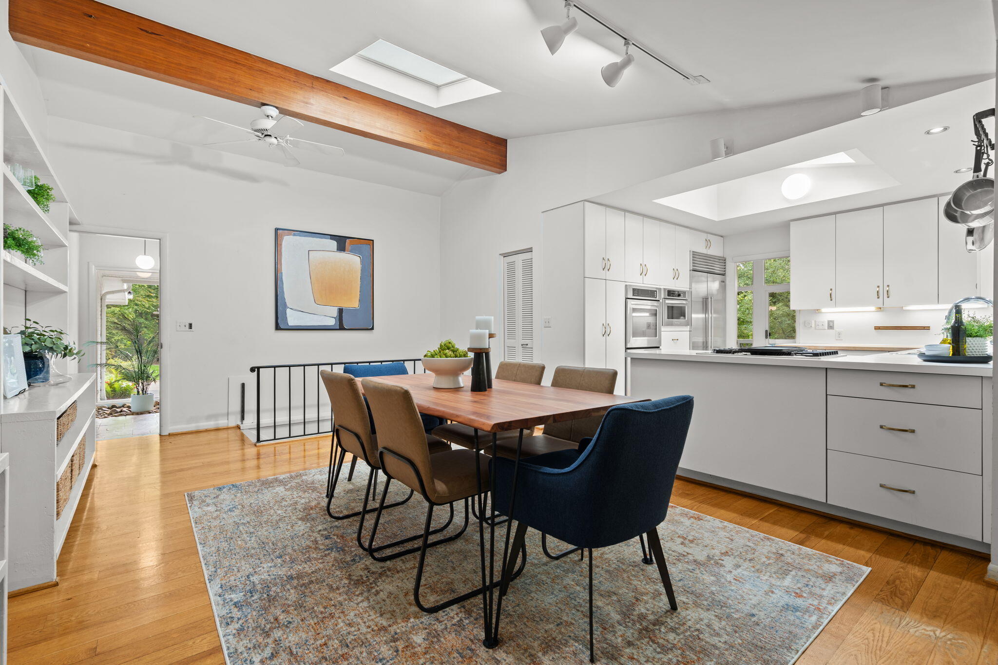 Dining area and modern kitchen with a large island, skylights, and an exposed wood ceiling beam.