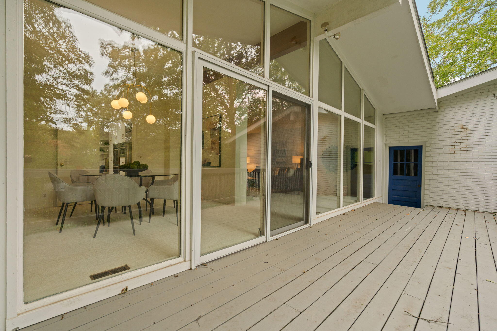 Wood deck beside floor-to-ceiling windows, with a blue door and dining area visible inside.