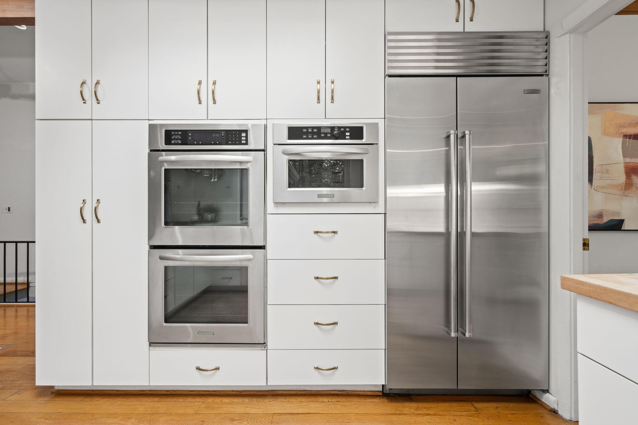Kitchen with white cabinetry, stacked stainless steel ovens, and a large stainless steel refrigerator.