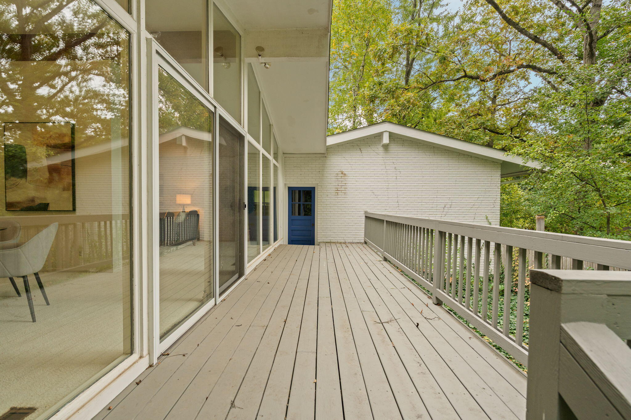 Elevated deck with gray plank flooring, sliding glass doors, and a leafy wooded view.