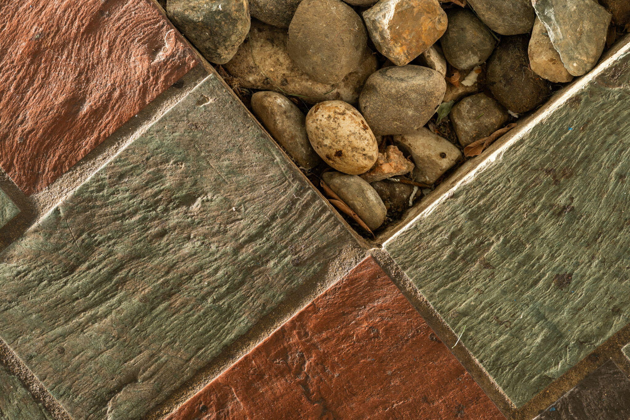 Stone walkway with red and green-gray pavers beside rounded river rocks.