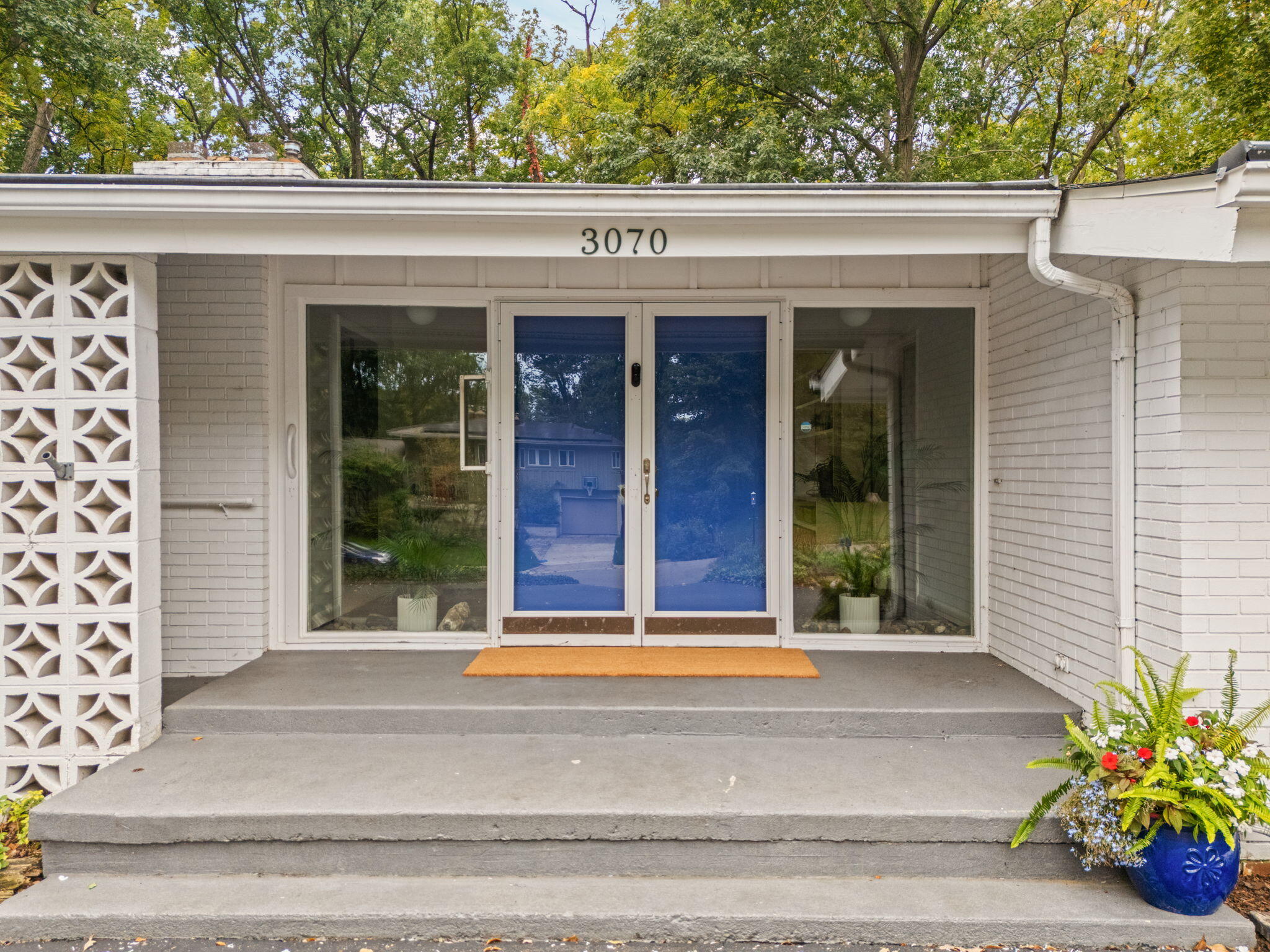 Front entrance with blue double doors, white brick, concrete steps, and a blue flower planter.