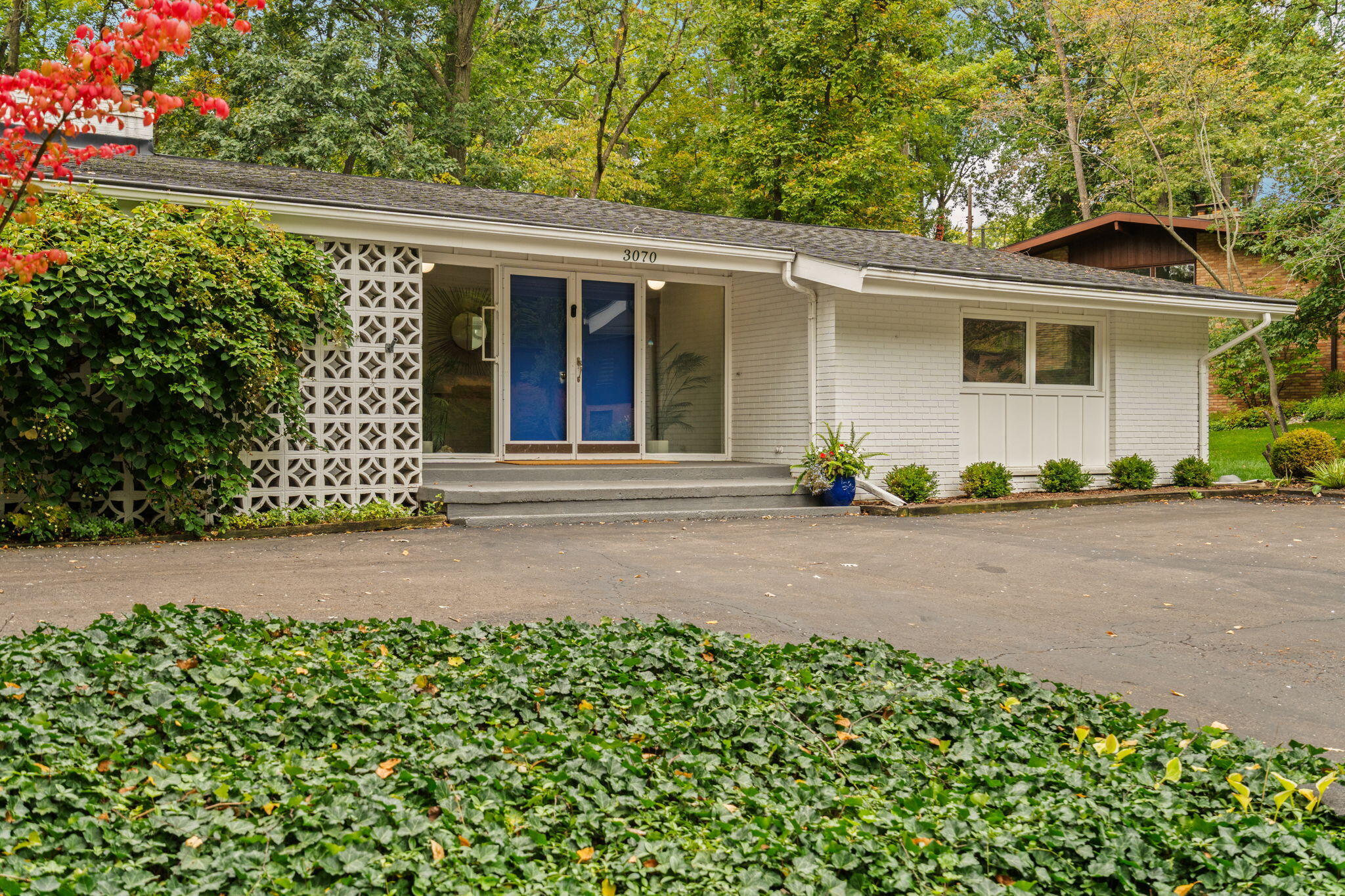 White brick home with blue double doors, decorative breeze-block screen, and ivy-covered landscaping.