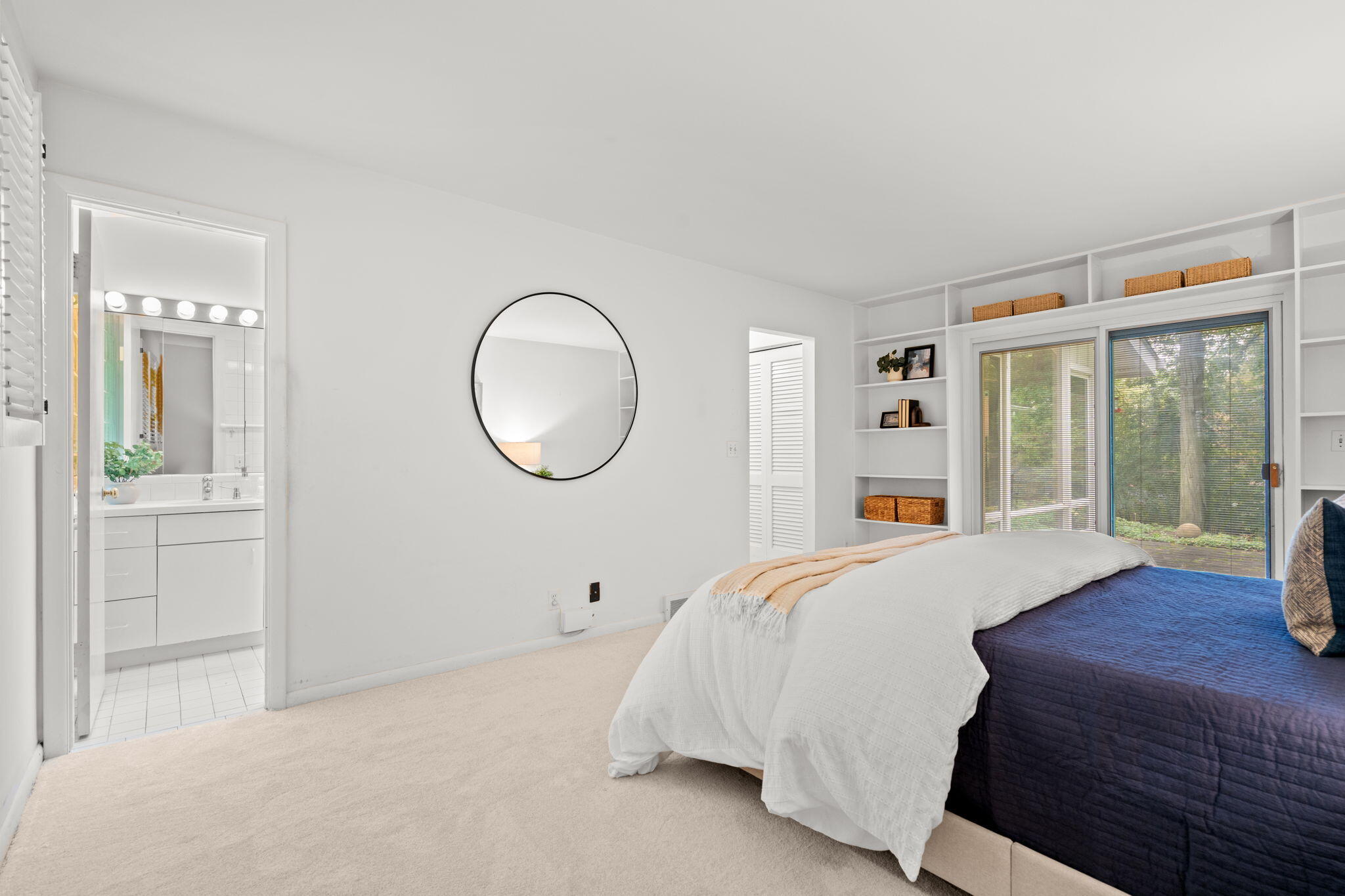 Bright bedroom with navy bedding, built-in shelves, and sliding glass doors overlooking trees.