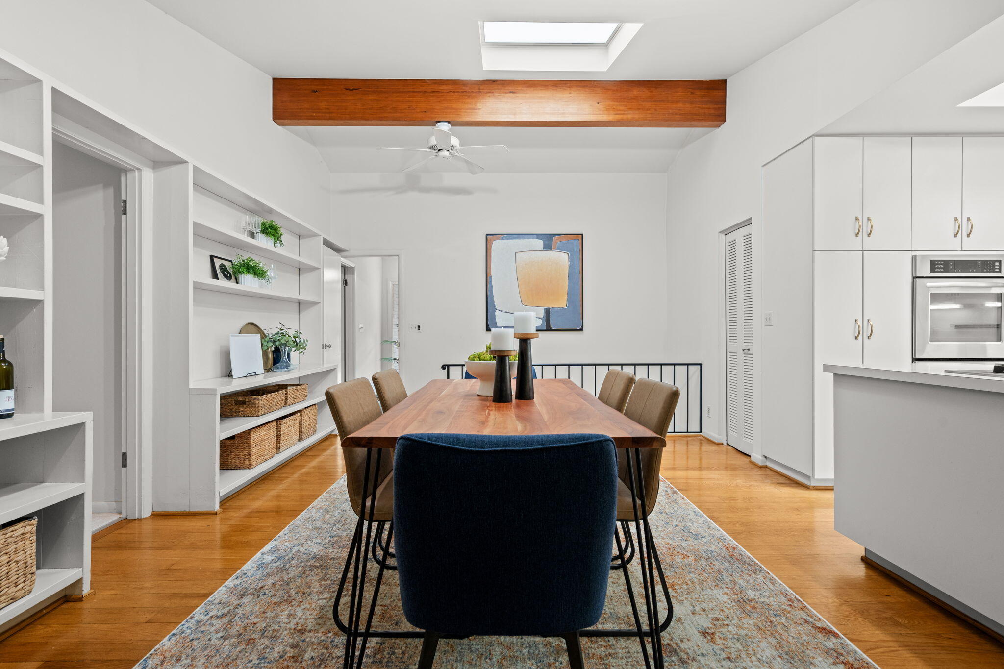 Dining room with a long wood table, built-in shelves, skylight and exposed ceiling beam.