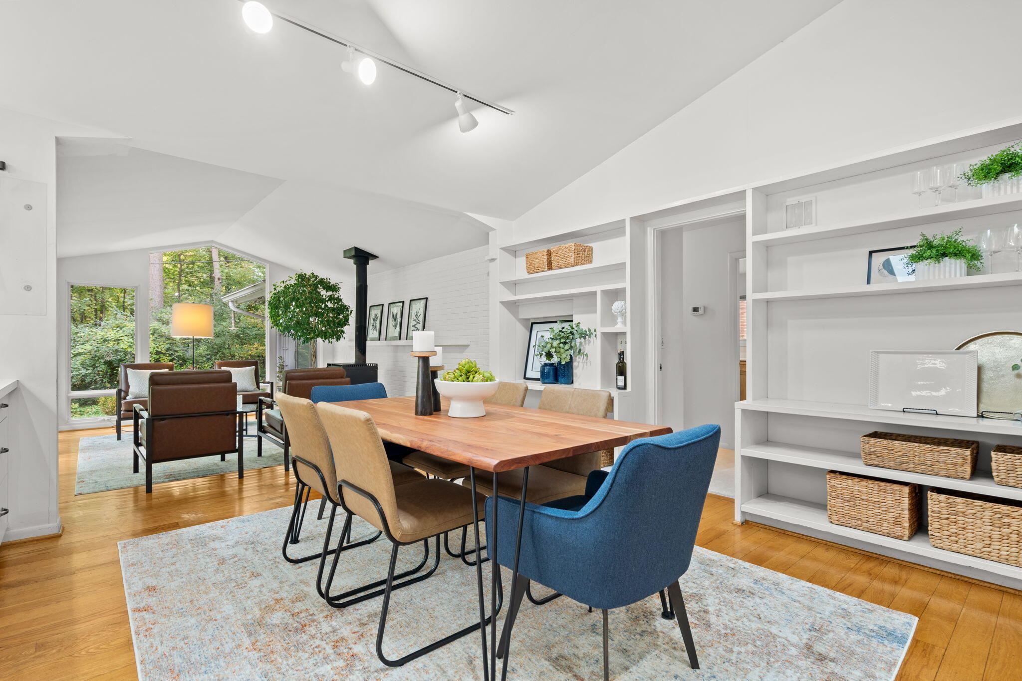 Open dining and living area with a long wood table, built-in shelves, and forest-facing windows.