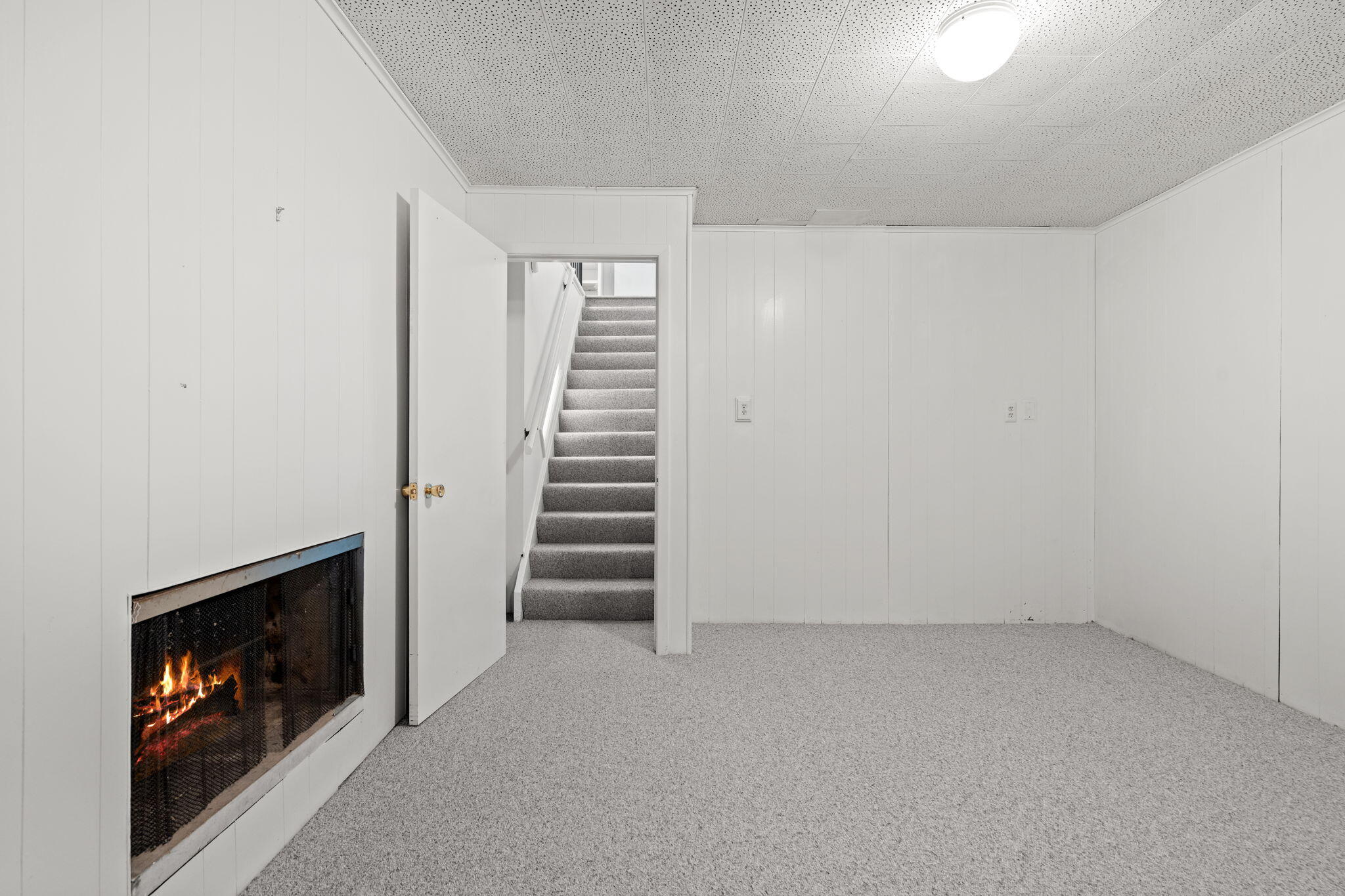 Empty basement room with a screened fireplace and carpeted stairs.