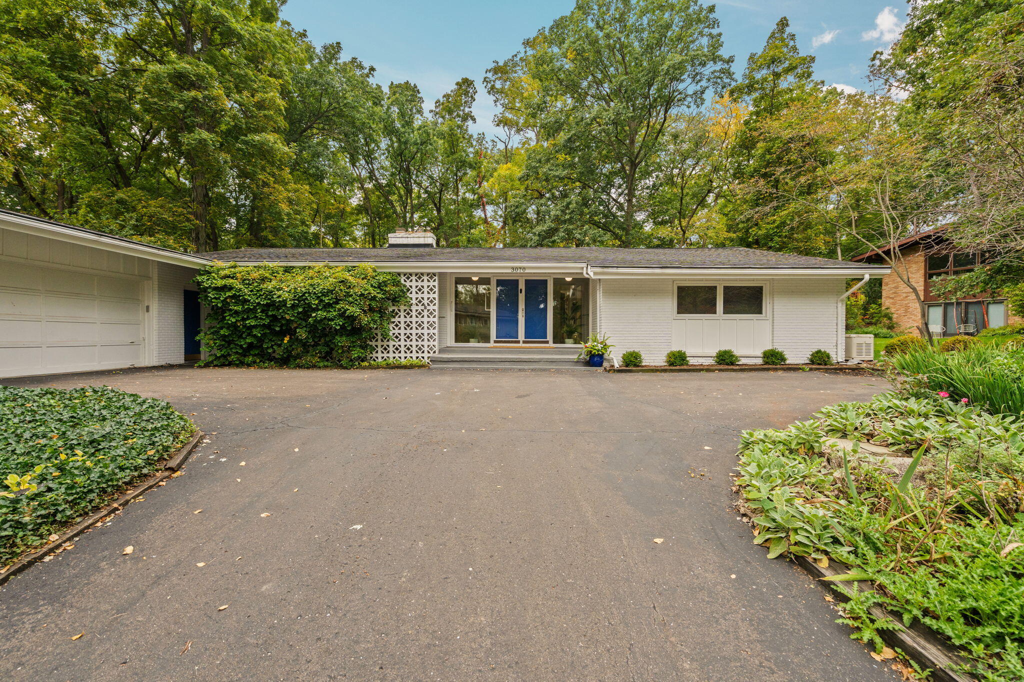 Single-story white house with blue entry doors, attached garage, and a broad paved driveway.